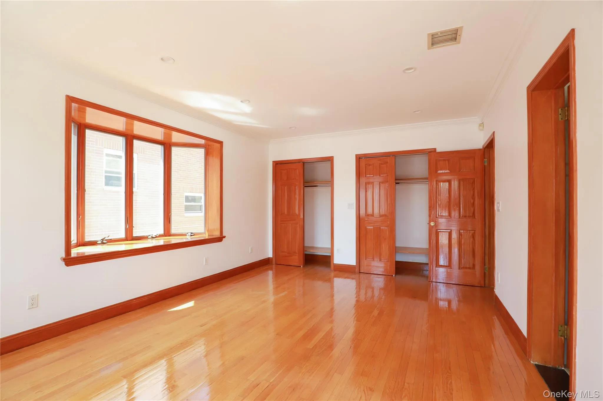 Spacious room featuring a bay window, wood-finish flooring, recessed lighting, and multiple closets with paneled wood doors Spacious room featuring a bay window, wood-finish flooring, recessed lighting, and multiple closets with paneled wood doors