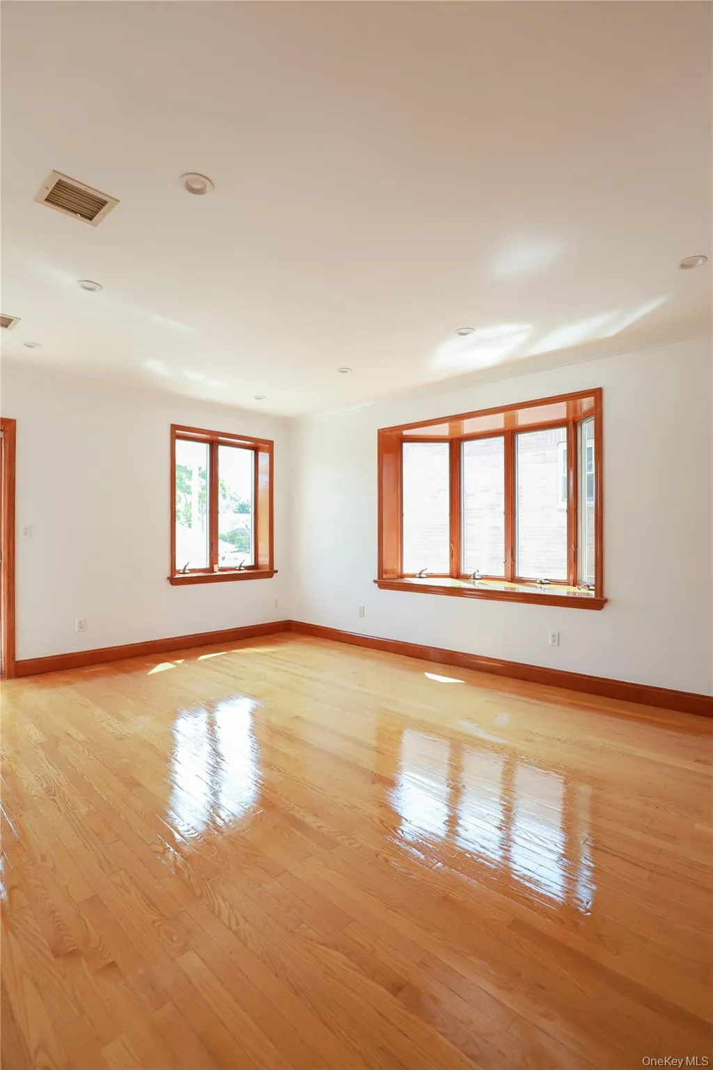 Bright interior space featuring polished wood flooring, a multi-pane bay window, two additional large windows, recessed ceiling lighting, and crisp white walls with wood trim Bright interior space featuring polished wood flooring, a multi-pane bay window, two additional large windows, recessed ceiling lighting, and crisp white walls with wood trim