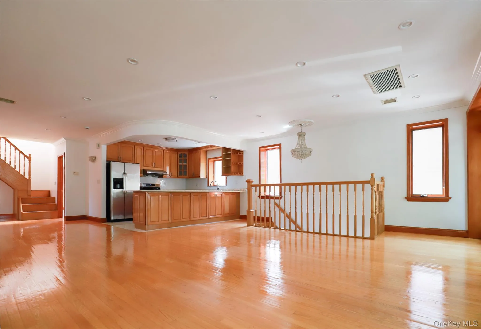 Open-concept living space featuring wood-finish flooring, a kitchen with wood cabinetry and stainless steel appliances, a hardwood staircase, and multiple windows with wood trim Open-concept living space featuring wood-finish flooring, a kitchen with wood cabinetry and stainless steel appliances, a hardwood staircase, and multiple windows with wood trim