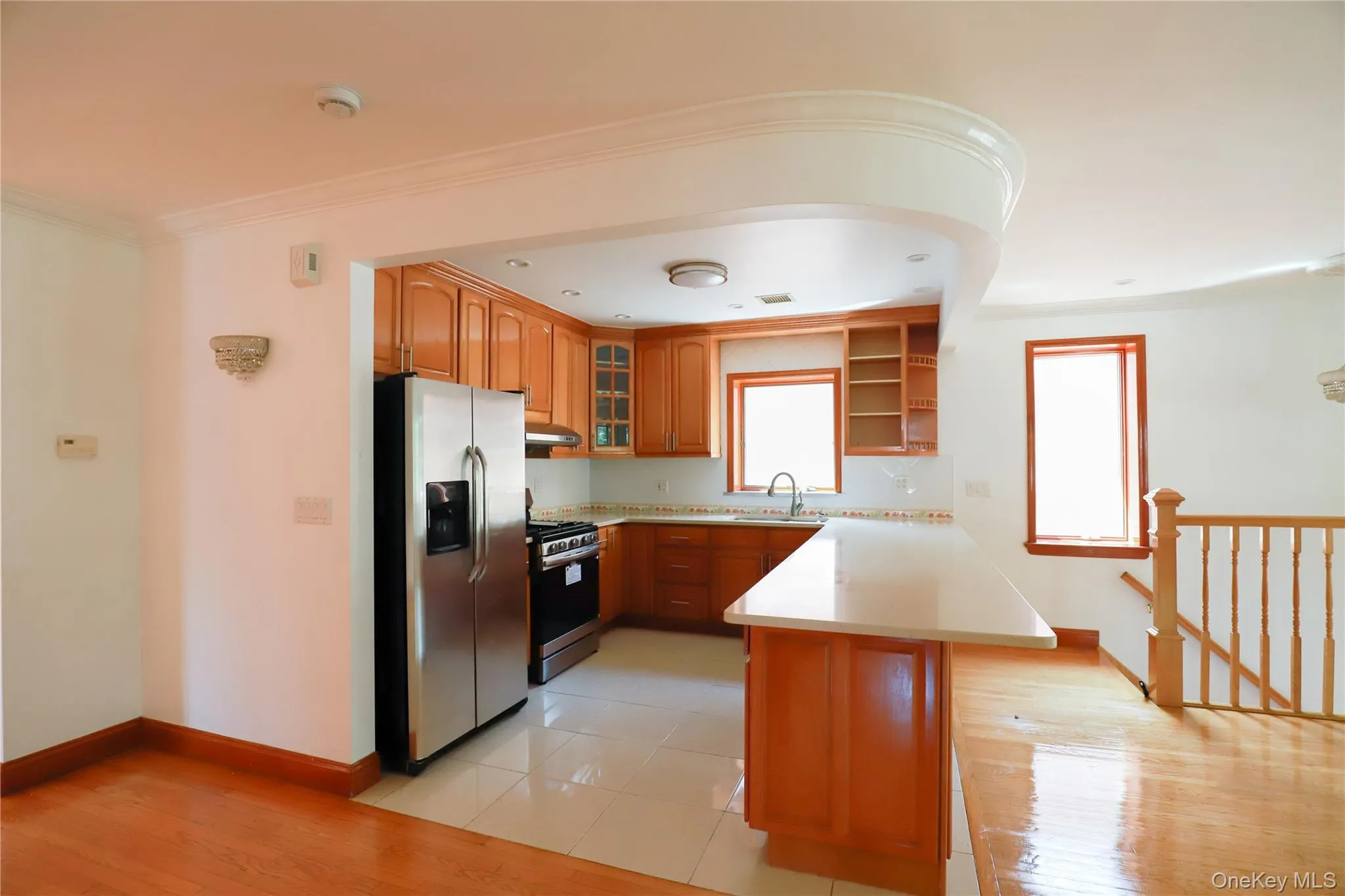 Kitchen featuring wood cabinetry, stainless steel appliances, white tile flooring, light-toned countertops, and a tile backsplash Kitchen featuring wood cabinetry, stainless steel appliances, white tile flooring, light-toned countertops, and a tile backsplash