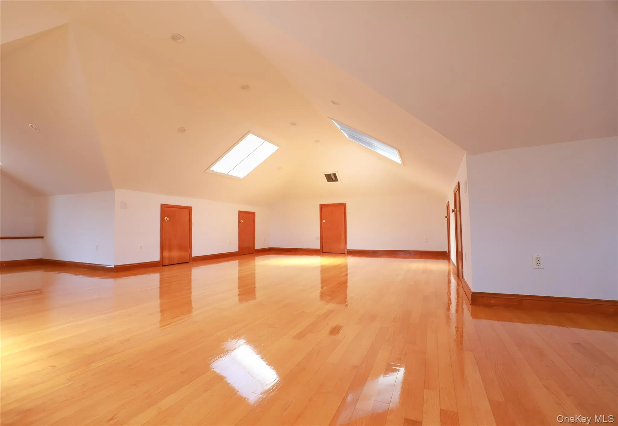 Spacious attic room featuring wood-finish flooring, multiple skylights, recessed lighting, and a vaulted ceiling Spacious attic room featuring wood-finish flooring, multiple skylights, recessed lighting, and a vaulted ceiling