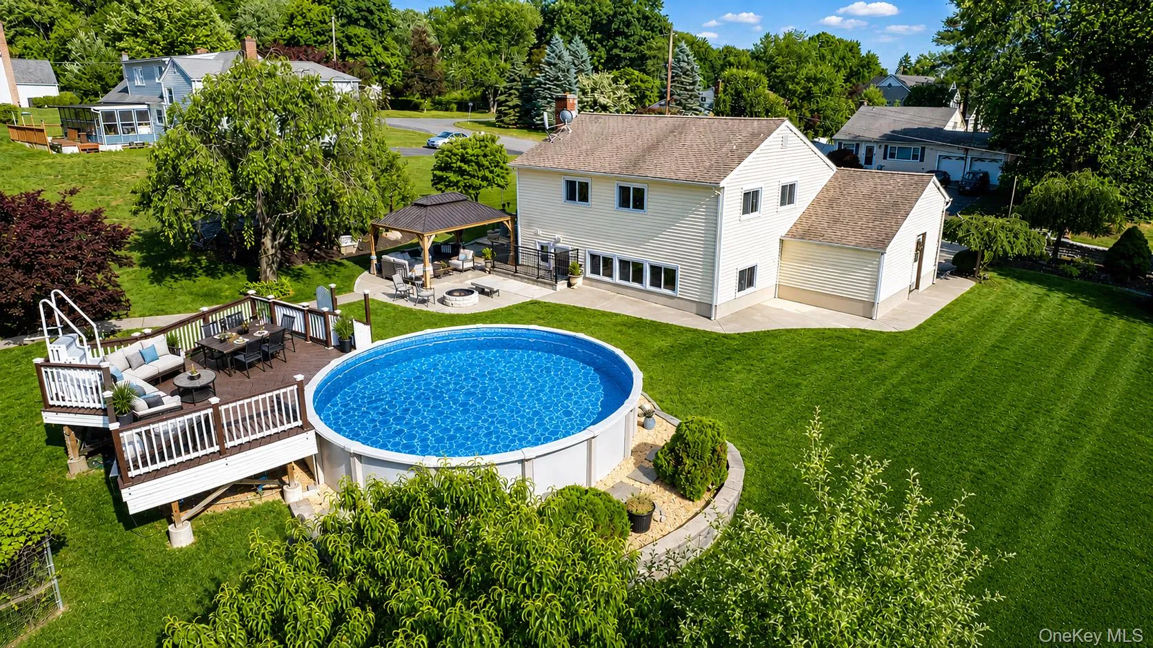 Expansive backyard featuring deck, above-ground pool, charming gazebo, fire pit area, and a manicured lawn Expansive backyard featuring deck, above-ground pool, charming gazebo, fire pit area, and a manicured lawn