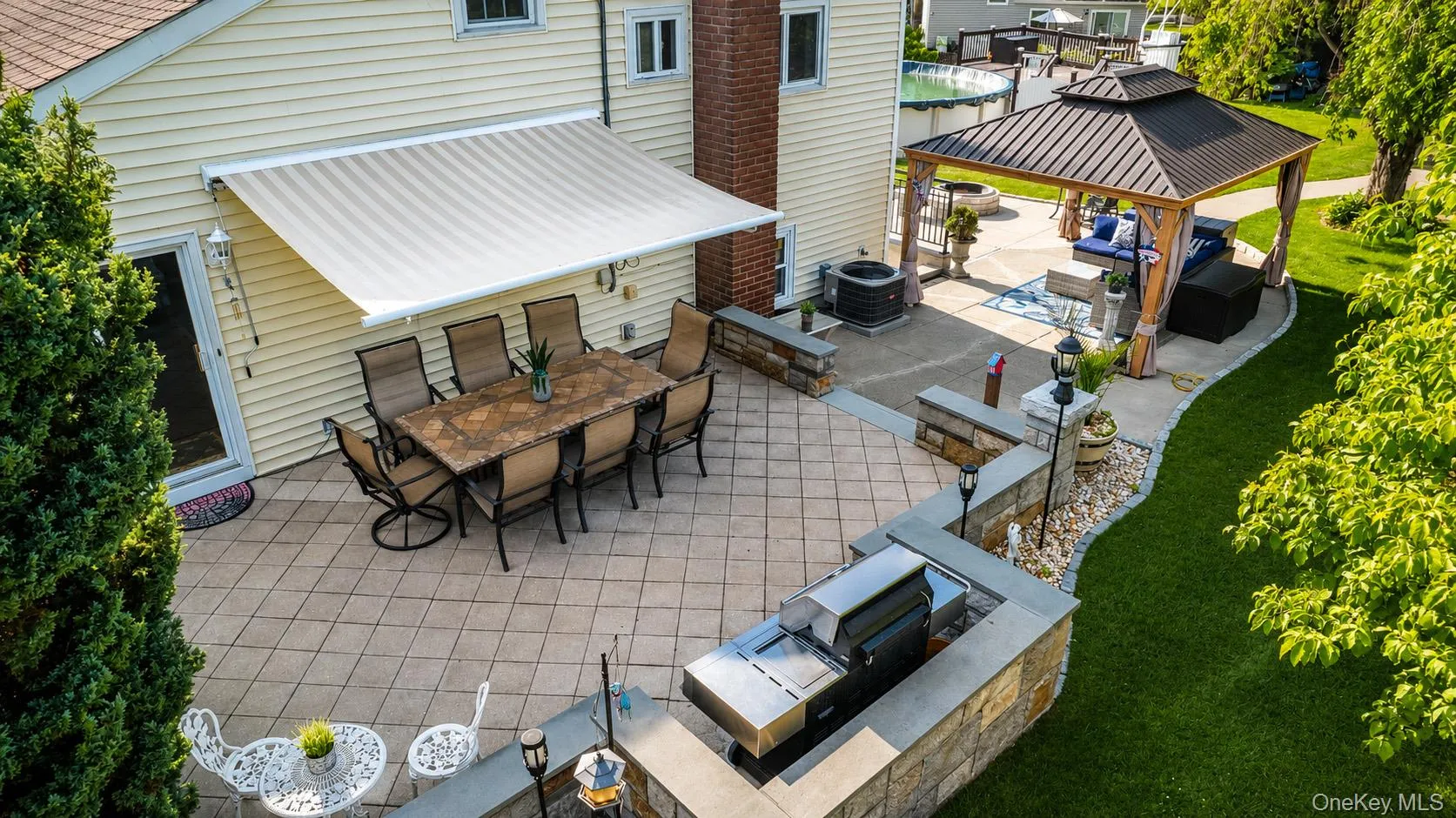 Expansive outdoor living area featuring a paved patio, built-in stone grill station, and a covered gazebo Expansive outdoor living area featuring a paved patio, built-in stone grill station, and a covered gazebo