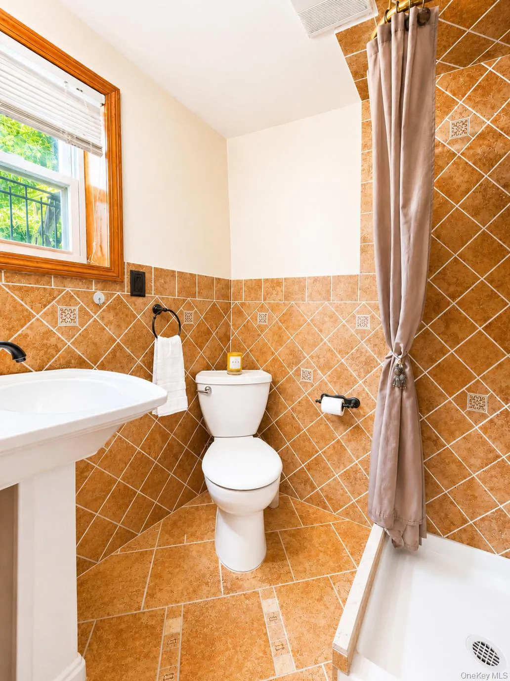 Bathroom featuring extensive terracotta-toned tilework with diamond-patterned accents and a pedestal sink Bathroom featuring extensive terracotta-toned tilework with diamond-patterned accents and a pedestal sink