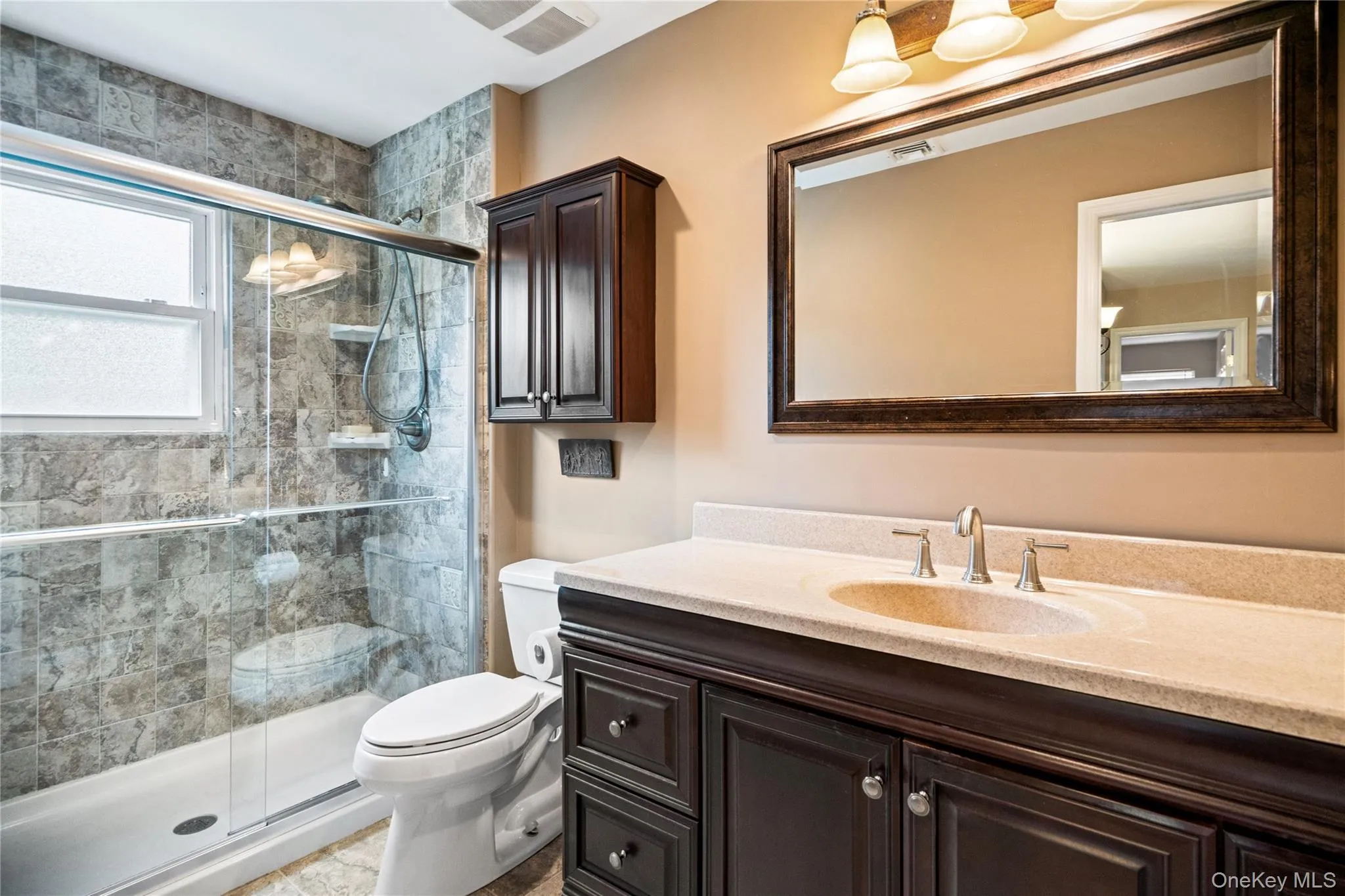 Full bathroom featuring a dark wood-finish vanity with a light-colored countertop, an undermount sink, and a framed mirror Full bathroom featuring a dark wood-finish vanity with a light-colored countertop, an undermount sink, and a framed mirror