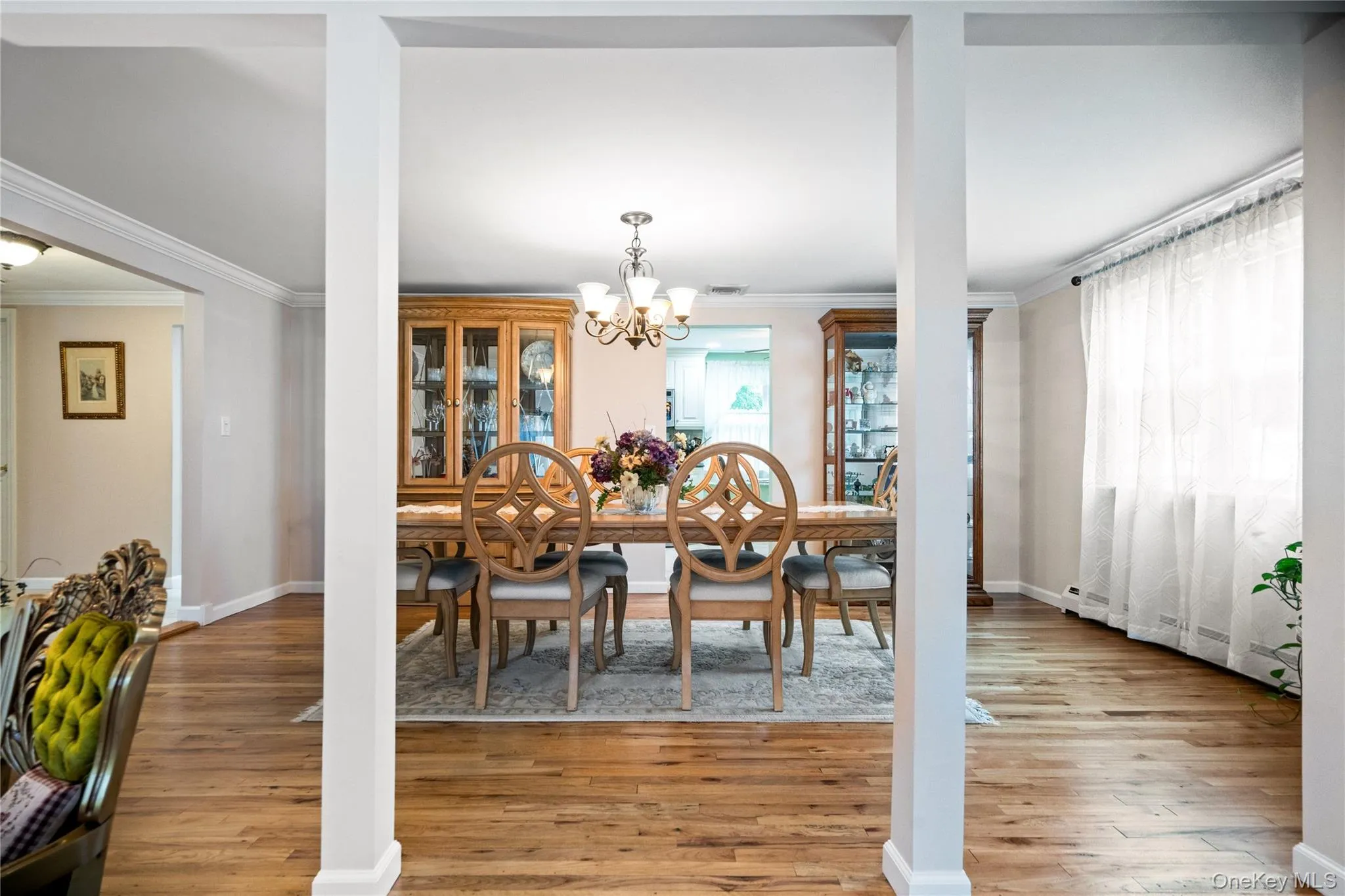 Dining area featuring wood-finish flooring, crown molding, a chandelier, and a large window with sheer curtains Dining area featuring wood-finish flooring, crown molding, a chandelier, and a large window with sheer curtains