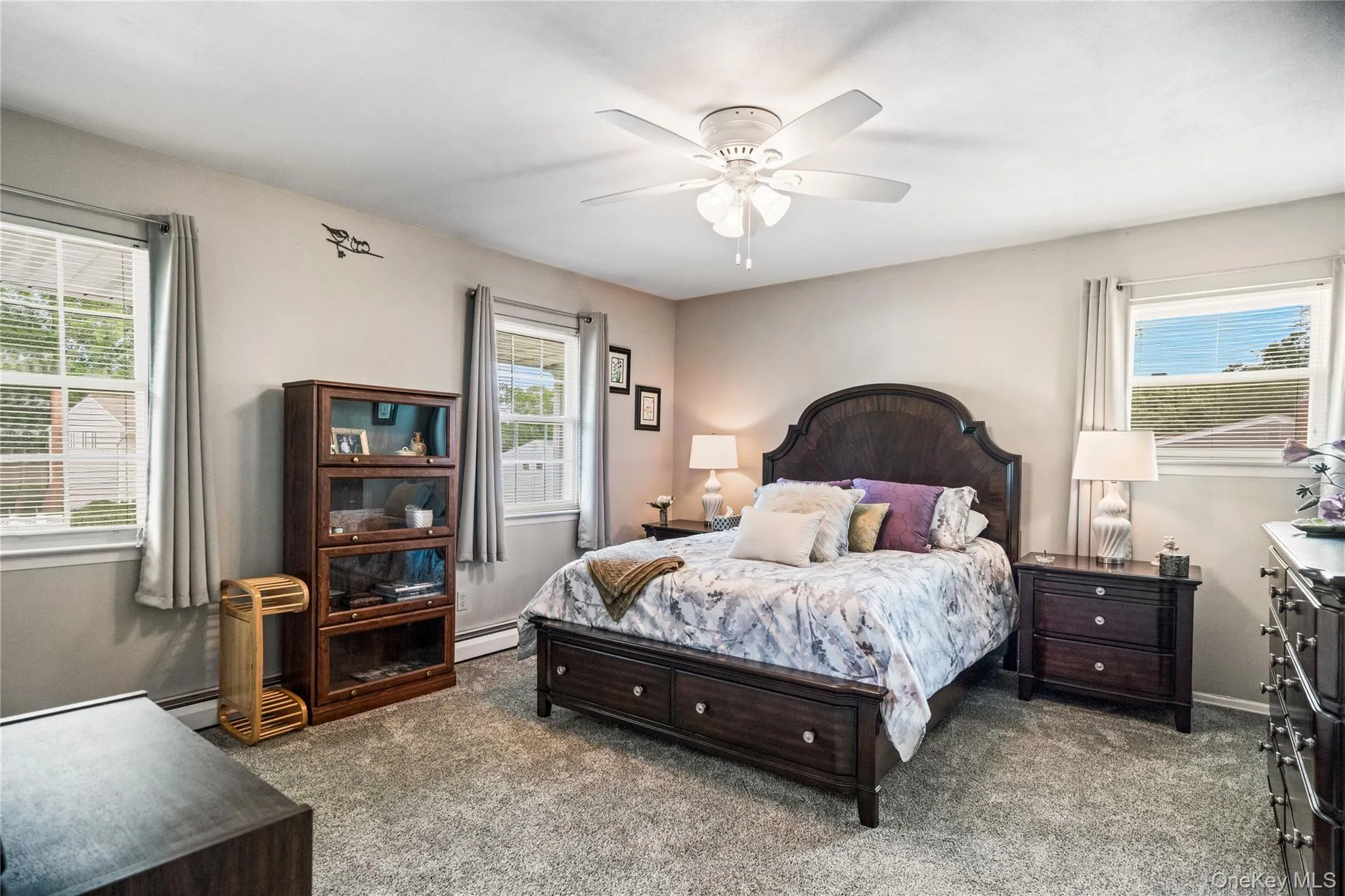 Carpeted room featuring a ceiling fan with light fixture, multiple windows with blinds, and neutral wall tones Carpeted room featuring a ceiling fan with light fixture, multiple windows with blinds, and neutral wall tones