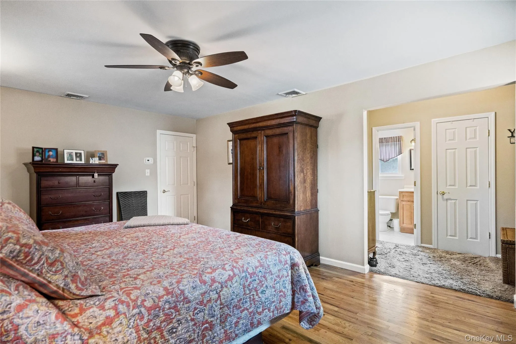 Bedroom featuring wood-finish flooring, a ceiling fan with integrated lighting, and a doorway opening to a bathroom with a window Bedroom featuring wood-finish flooring, a ceiling fan with integrated lighting, and a doorway opening to a bathroom with a window