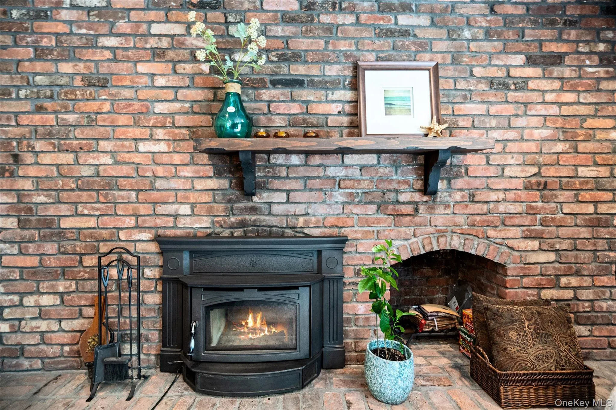 Exposed brick wall featuring a cast iron fireplace insert, a distressed wood-finish mantel, and an arched brick alcove Exposed brick wall featuring a cast iron fireplace insert, a distressed wood-finish mantel, and an arched brick alcove