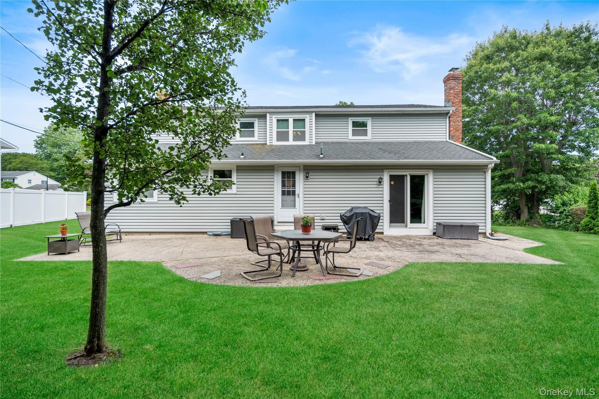 Expansive rear yard featuring a patterned concrete patio, mature trees, and a white privacy fence Expansive rear yard featuring a patterned concrete patio, mature trees, and a white privacy fence