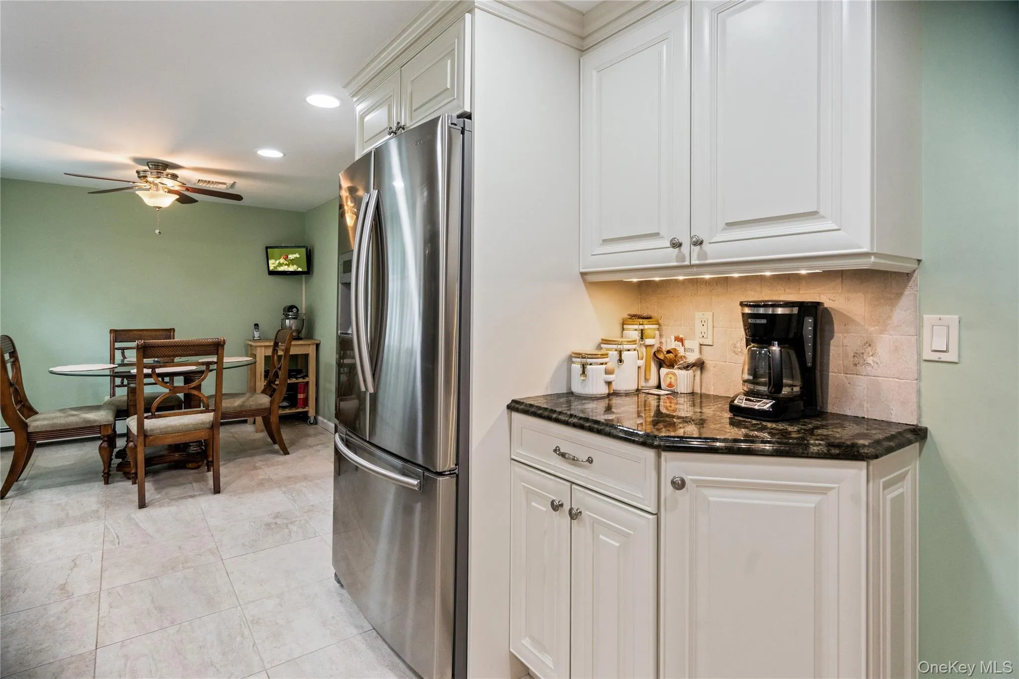 Kitchen area featuring white cabinetry, dark countertop, stainless steel refrigerator, and tiled flooring Kitchen area featuring white cabinetry, dark countertop, stainless steel refrigerator, and tiled flooring
