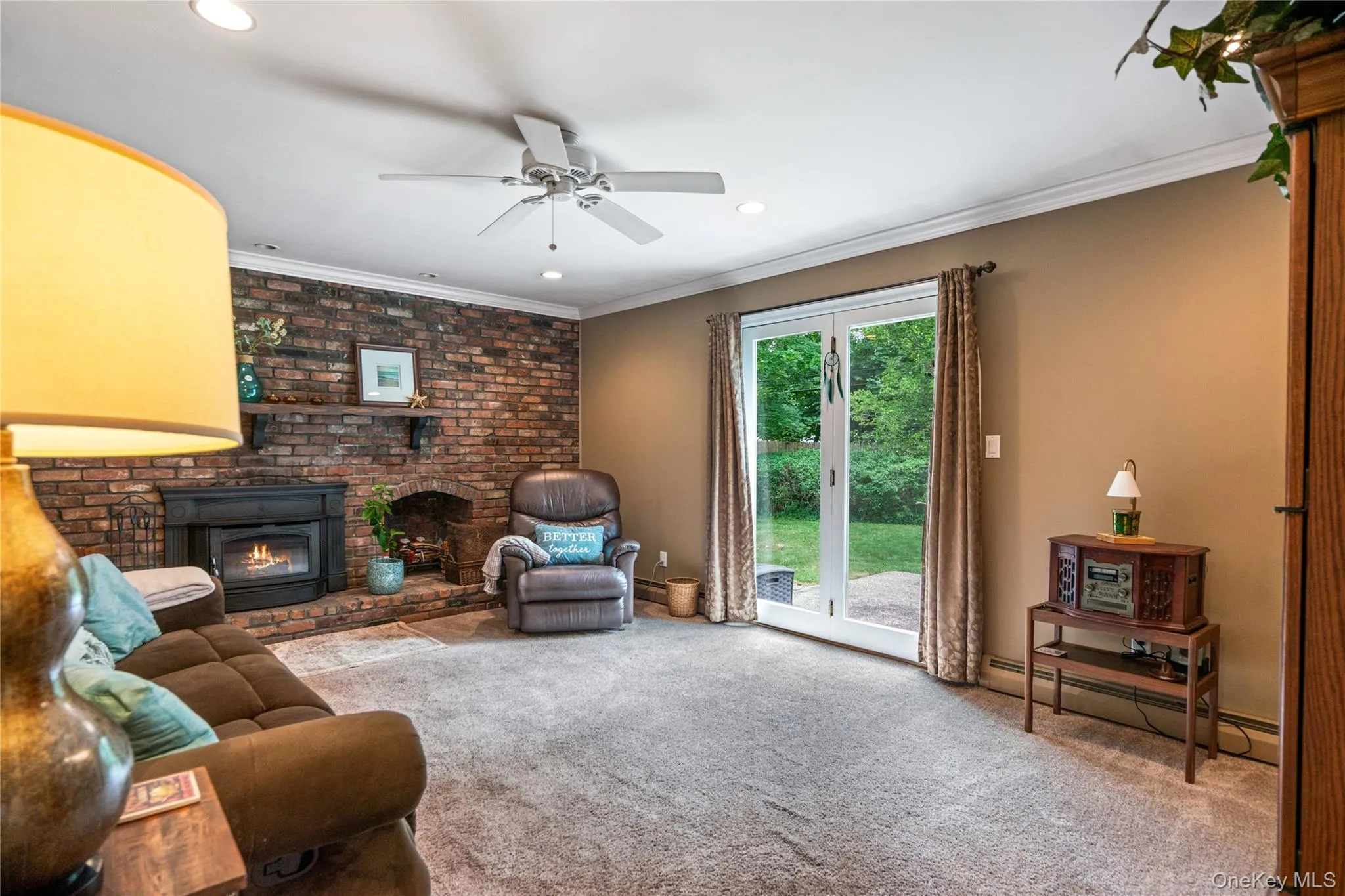 Living area featuring a full brick accent wall, a fireplace with a black insert, and a wood mantel Living area featuring a full brick accent wall, a fireplace with a black insert, and a wood mantel