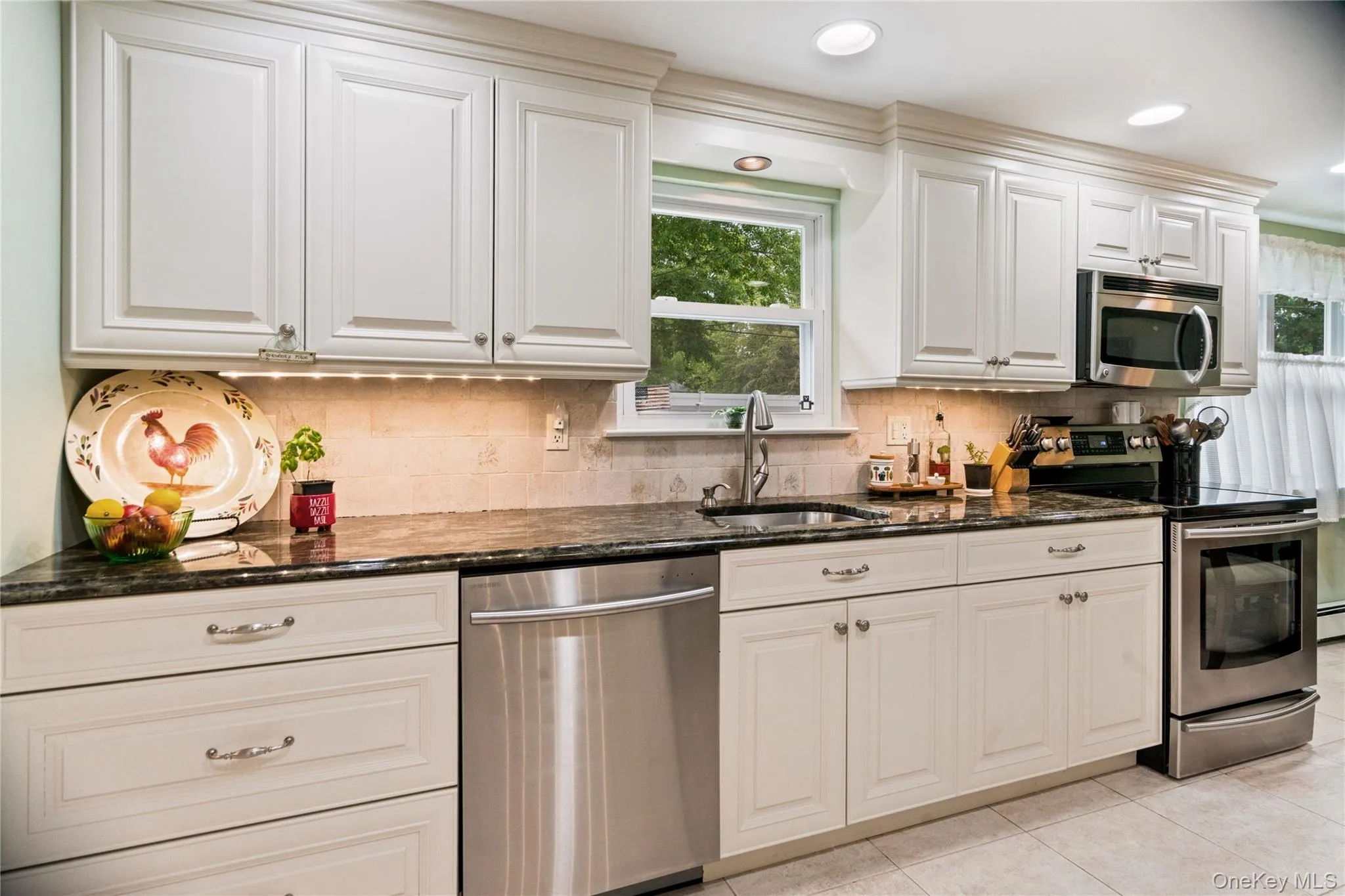 Kitchen featuring white cabinetry with crown molding, dark stone countertops, stainless steel appliances, a tile backsplash, and recessed lighting Kitchen featuring white cabinetry with crown molding, dark stone countertops, stainless steel appliances, a tile backsplash, and recessed lighting