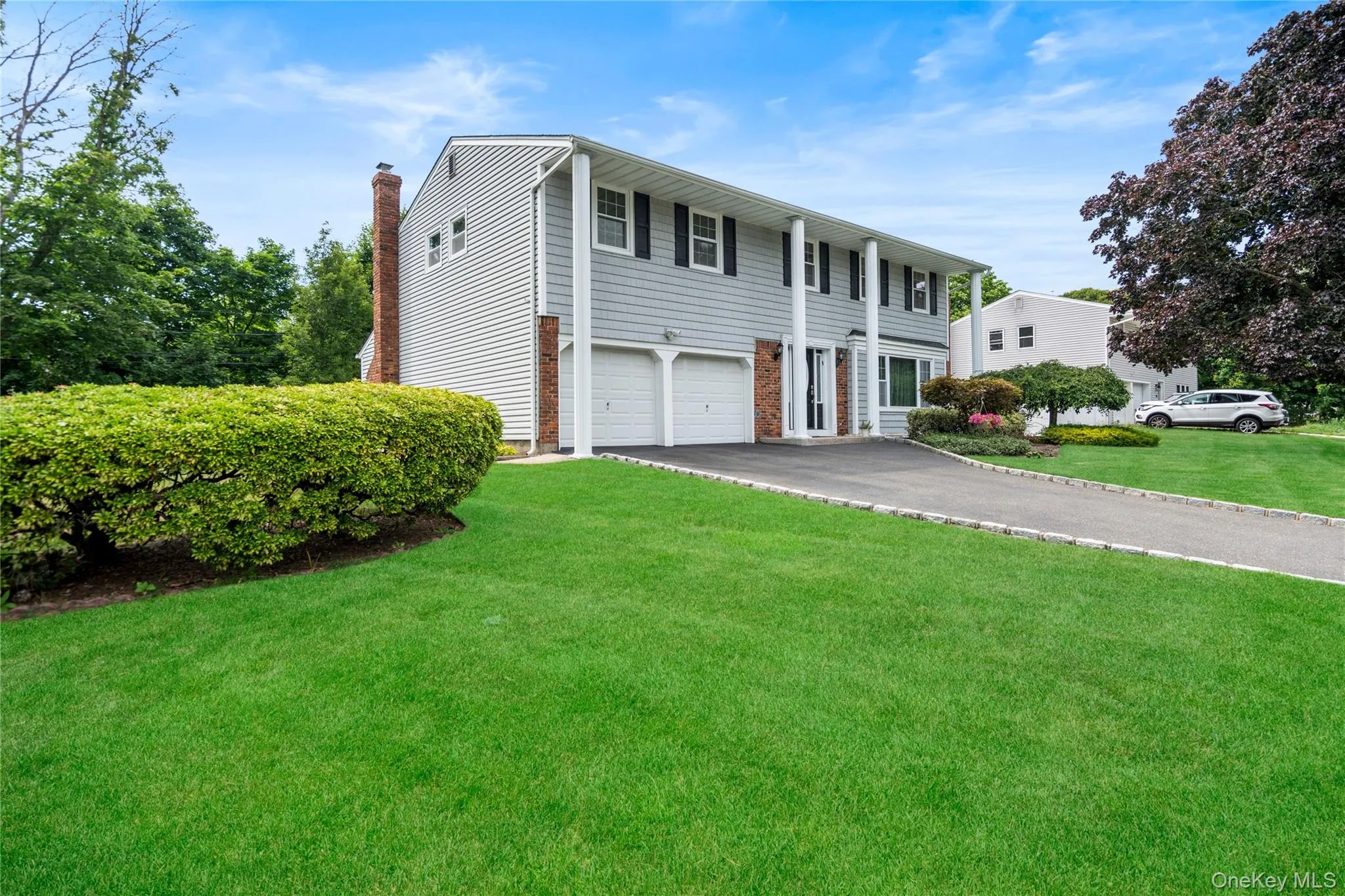 Colonial-style residence featuring light gray siding with white trim, black shutters, white support columns, and an integrated two-car garage Colonial-style residence featuring light gray siding with white trim, black shutters, white support columns, and an integrated two-car garage