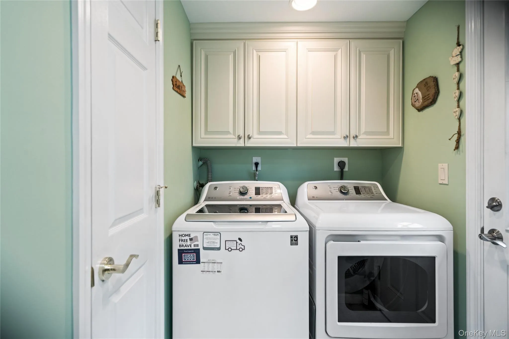 Dedicated laundry area featuring overhead cabinetry, light green wall finishes, and a light fixture Dedicated laundry area featuring overhead cabinetry, light green wall finishes, and a light fixture