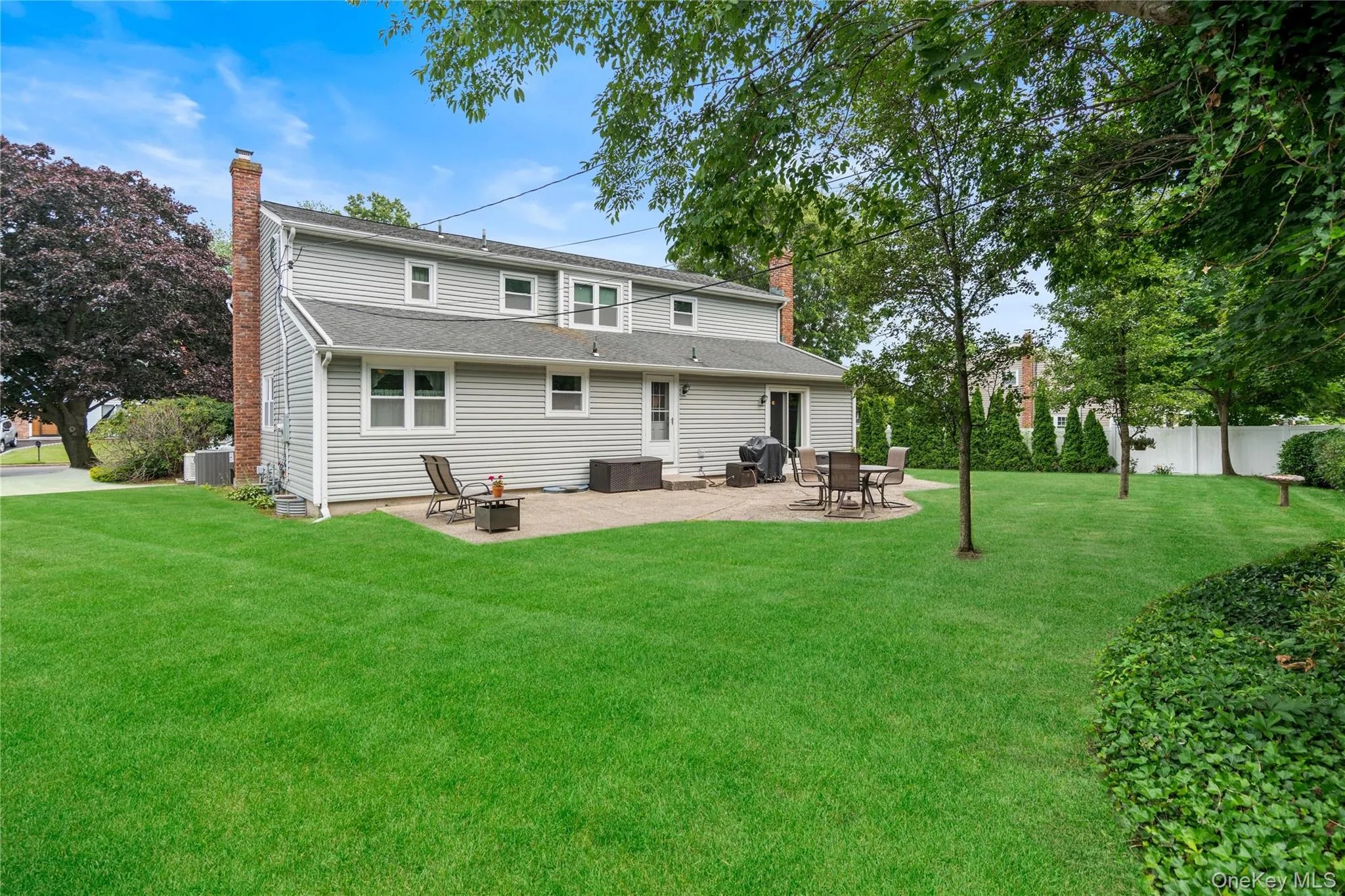 Spacious rear yard with a large patio area, extensive lawn, mature trees, privacy fencing, and brick chimney Spacious rear yard with a large patio area, extensive lawn, mature trees, privacy fencing, and brick chimney