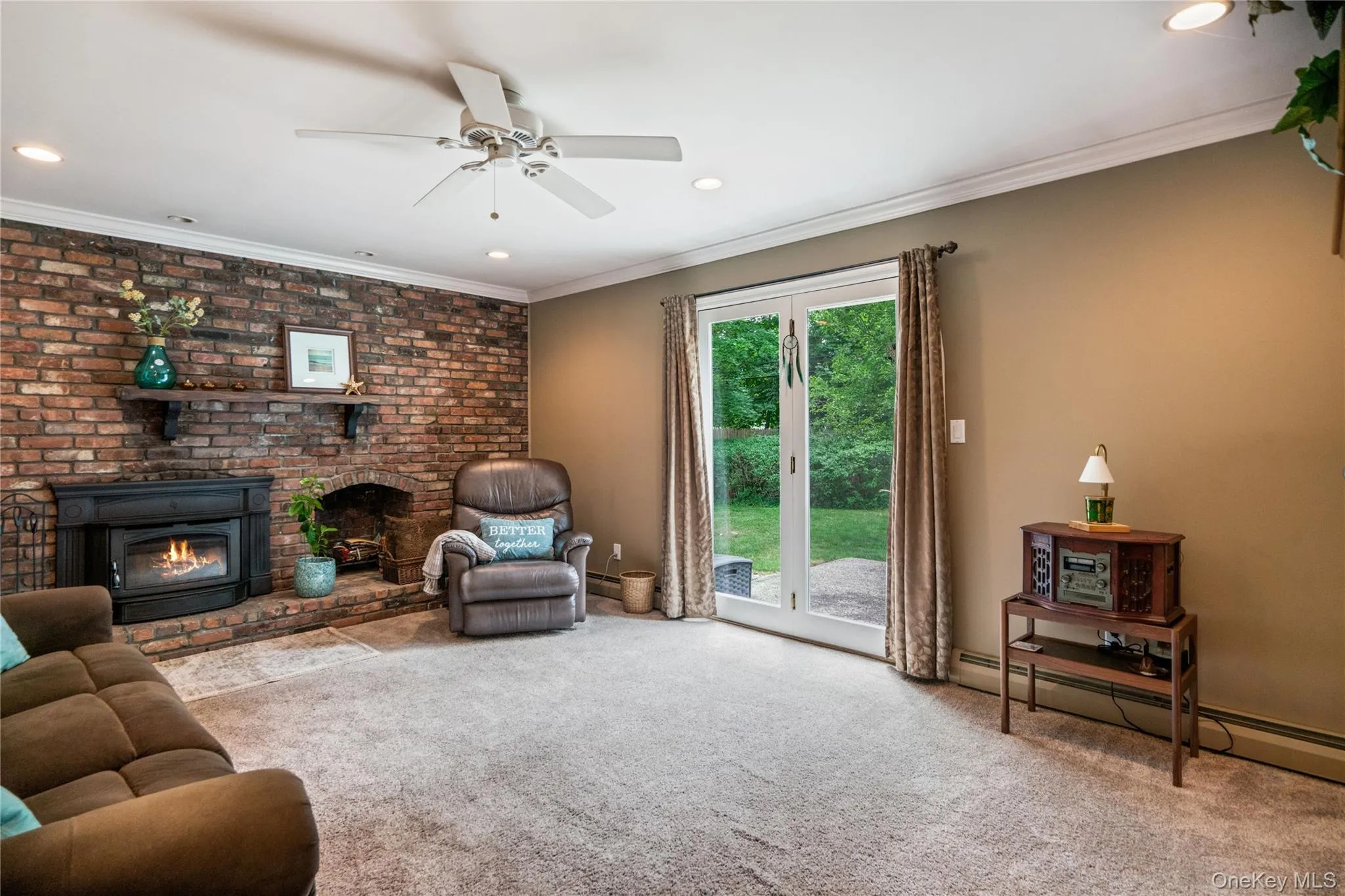 Carpeted room featuring a brick accent wall with a built-in fireplace insert and hearth Carpeted room featuring a brick accent wall with a built-in fireplace insert and hearth