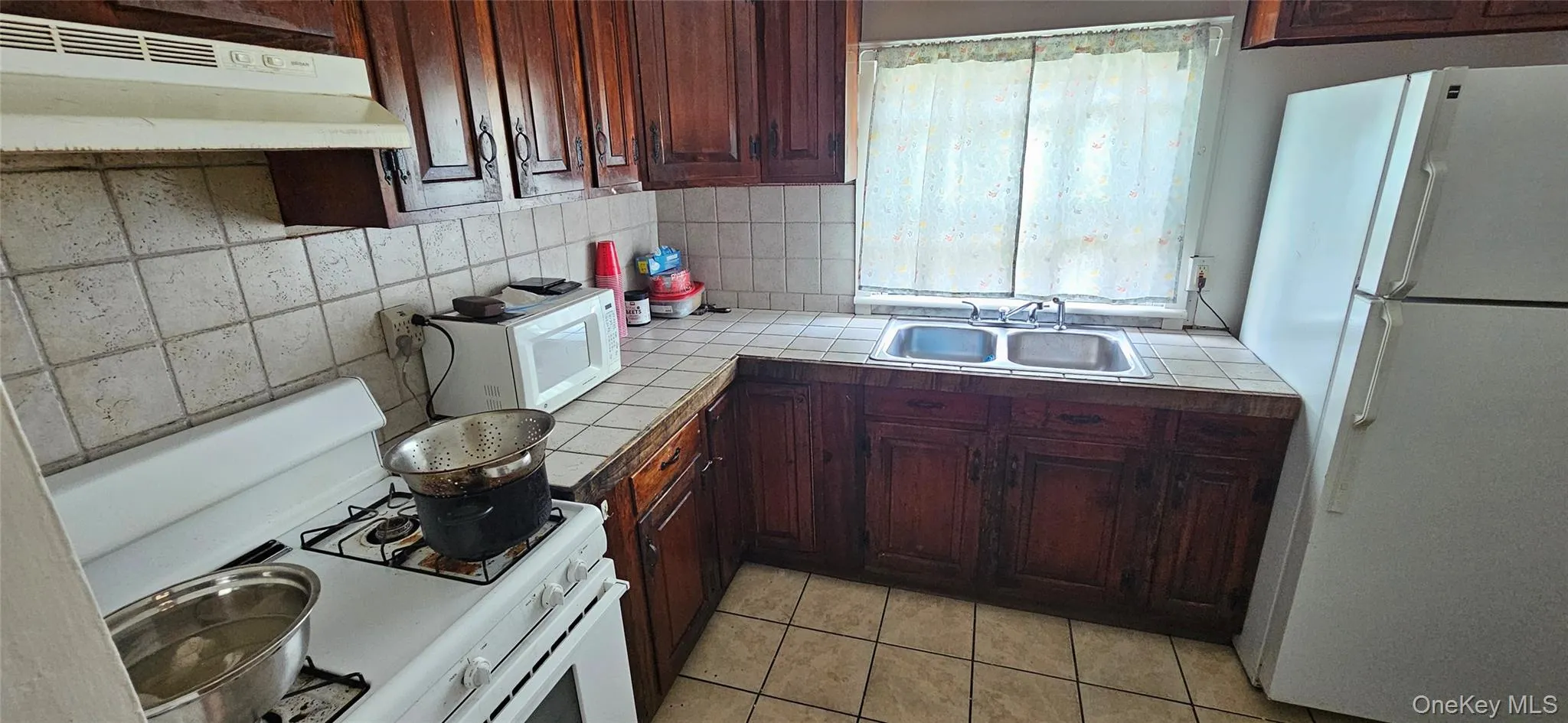 Kitchen featuring wood cabinetry, a tiled backsplash, and matching tile flooring Kitchen featuring wood cabinetry, a tiled backsplash, and matching tile flooring