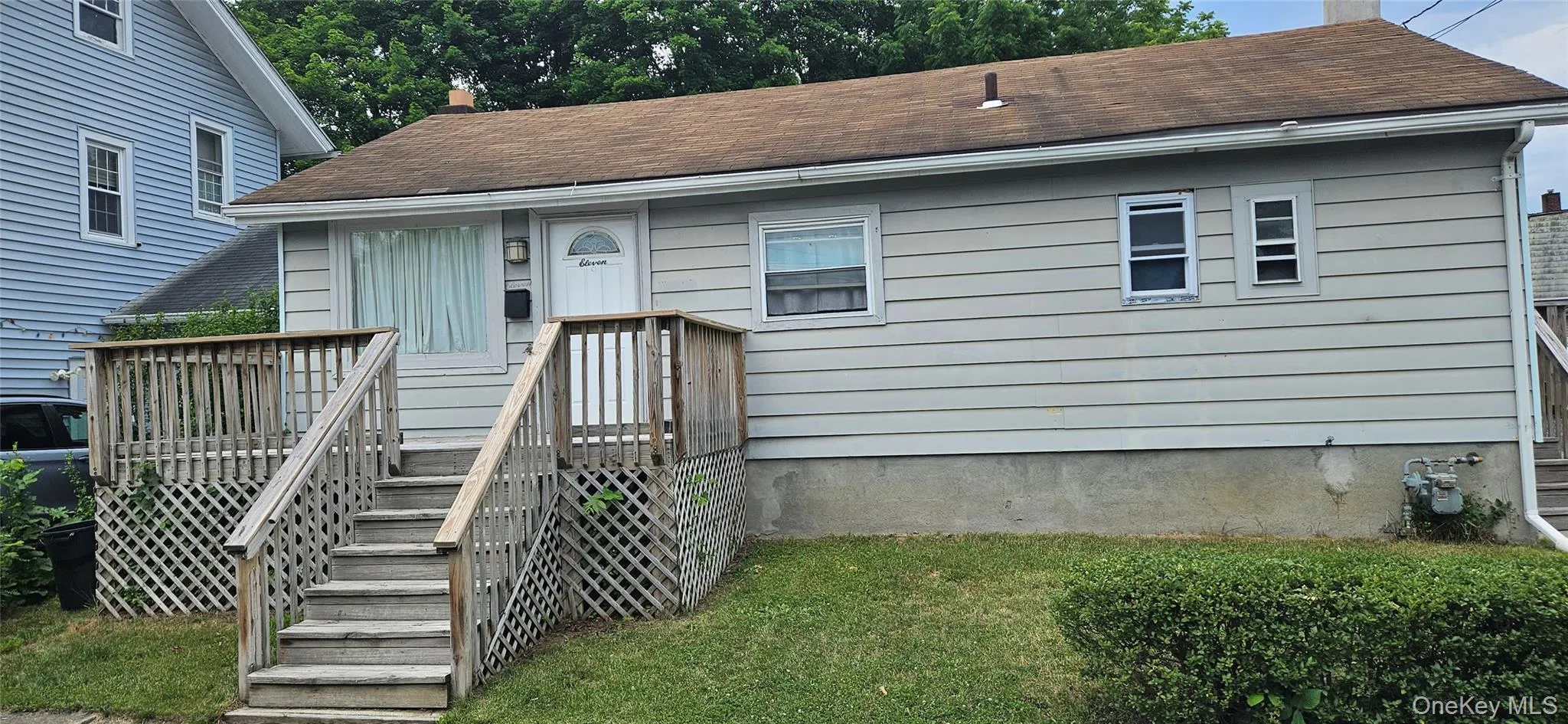 Single-story residence featuring light-colored siding, a front entry deck with railings, and established front yard landscaping Single-story residence featuring light-colored siding, a front entry deck with railings, and established front yard landscaping
