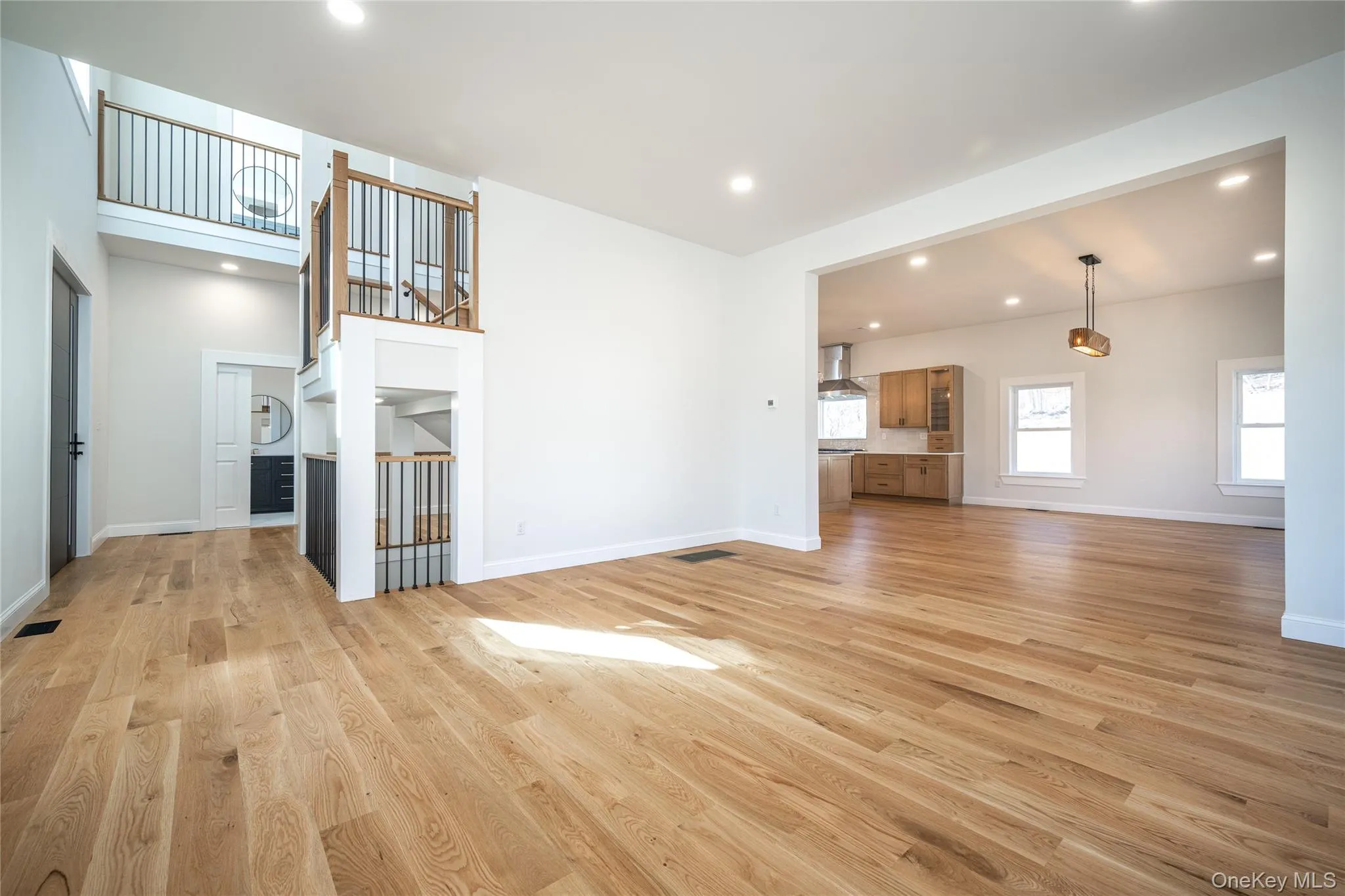 Expansive main living area featuring light wood-finish flooring, recessed lighting, and a multi-level staircase with dark metal balusters Expansive main living area featuring light wood-finish flooring, recessed lighting, and a multi-level staircase with dark metal balusters