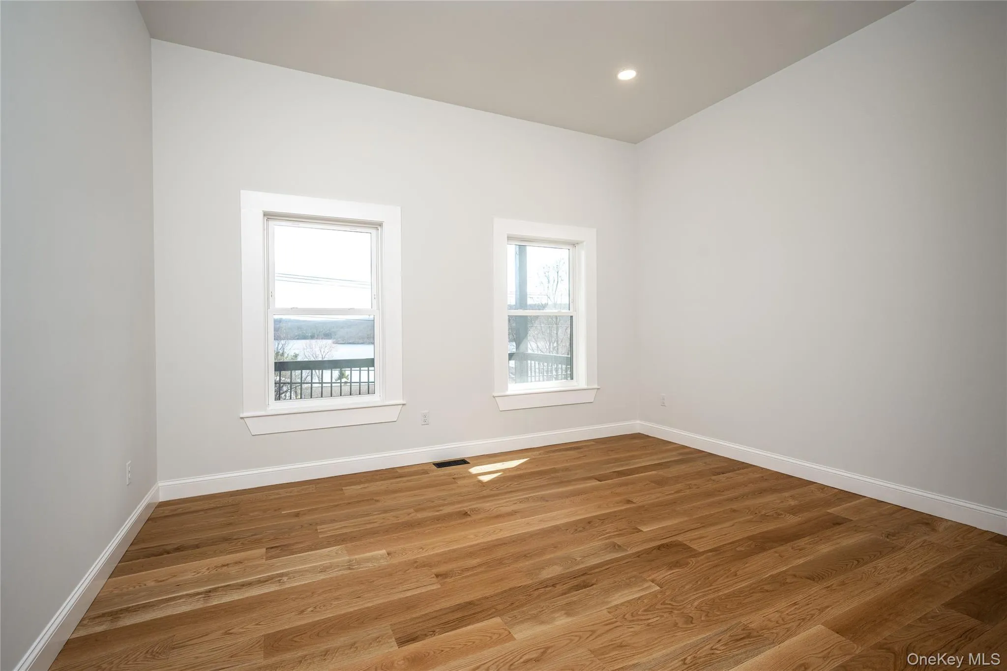 Bright room featuring two windows with white trim, wood-finish flooring, a recessed ceiling light, and light-toned walls Bright room featuring two windows with white trim, wood-finish flooring, a recessed ceiling light, and light-toned walls