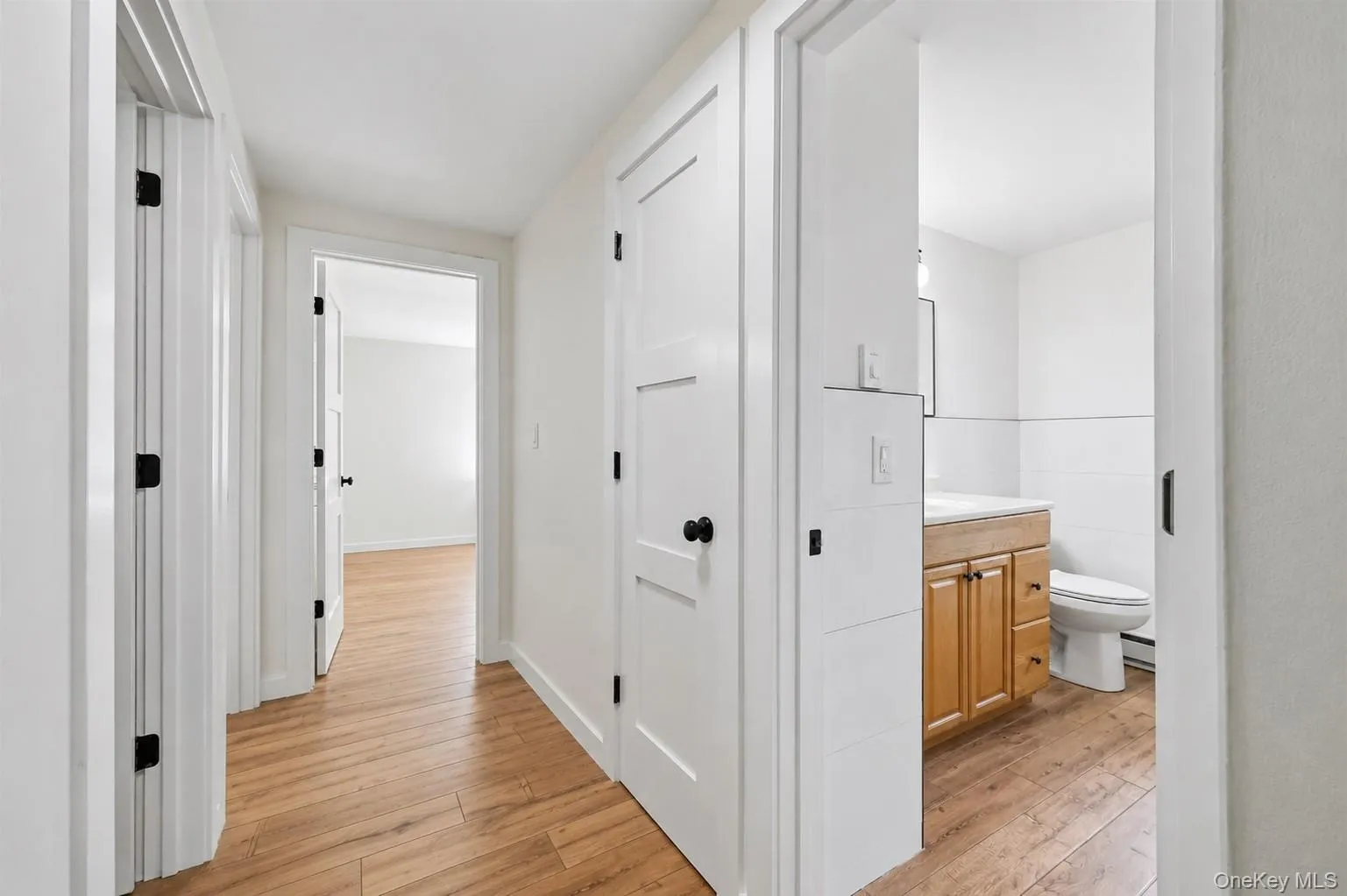 Hallway featuring wood-finish flooring, white walls, and white trim Hallway featuring wood-finish flooring, white walls, and white trim
