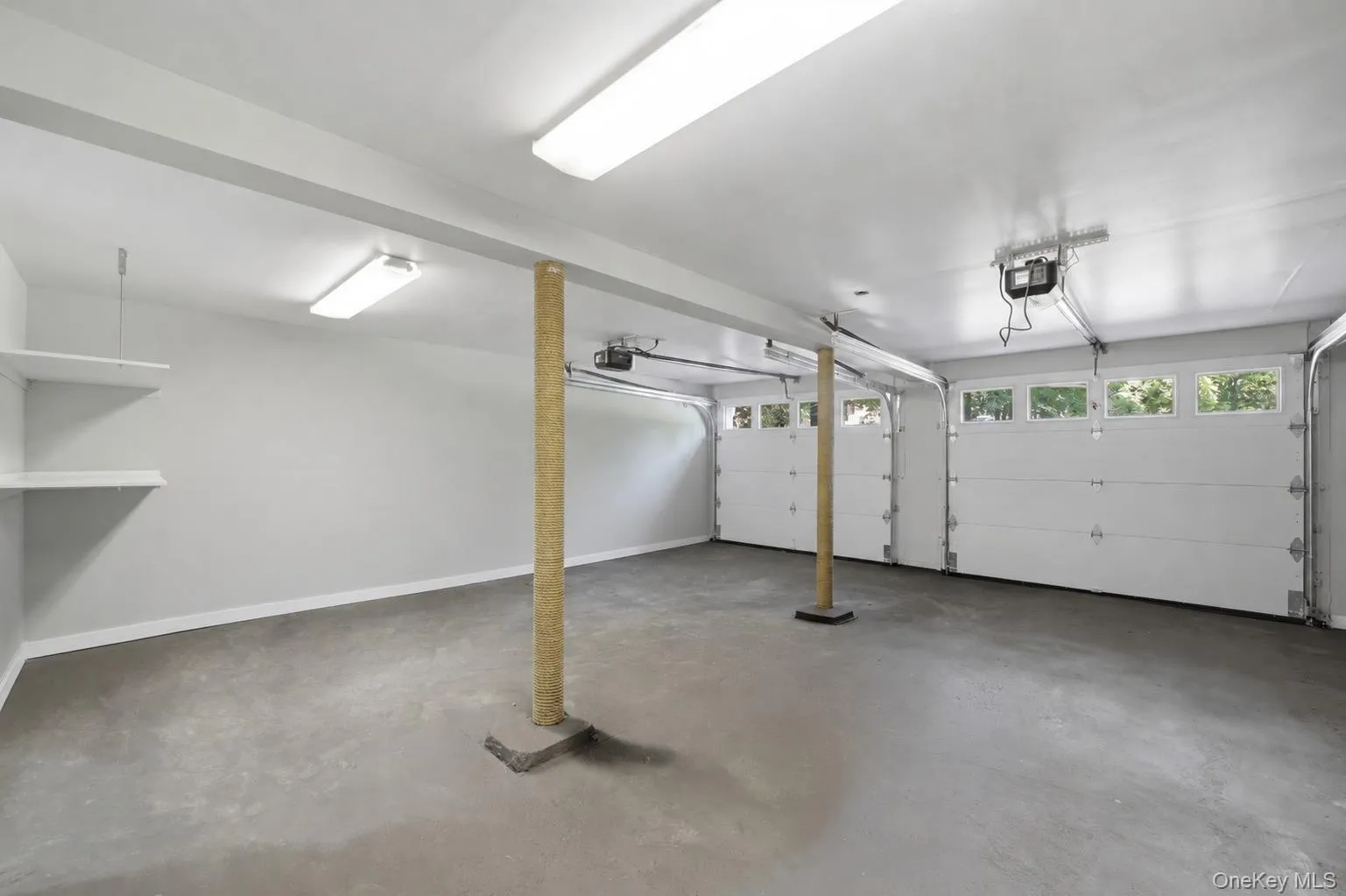 Spacious two-car garage featuring a concrete floor, white walls, and built-in shelving Spacious two-car garage featuring a concrete floor, white walls, and built-in shelving
