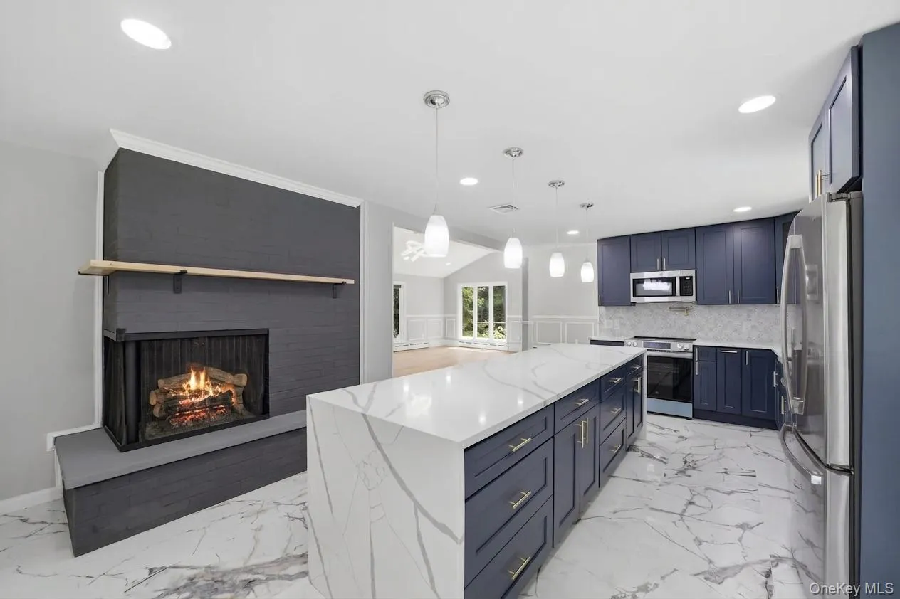 Spacious kitchen with a large waterfall island featuring a quartz countertop and navy cabinetry, complemented by stainless steel appliances, recessed lighting, and pendant lighting fixtures Spacious kitchen with a large waterfall island featuring a quartz countertop and navy cabinetry, complemented by stainless steel appliances, recessed lighting, and pendant lighting fixtures