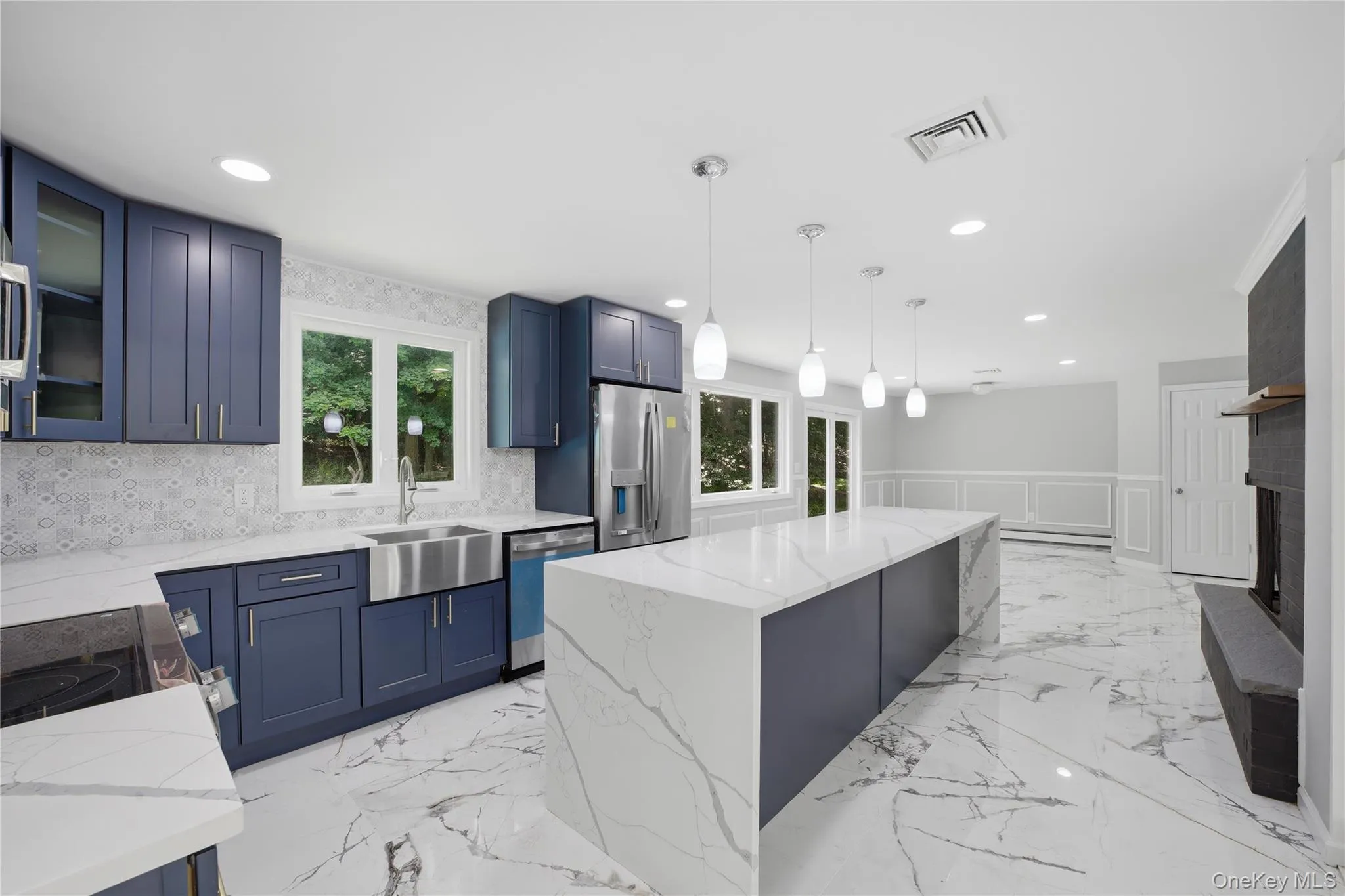 Open-concept kitchen featuring an expansive central island with a waterfall edge, quartz countertops, and blue shaker cabinetry Open-concept kitchen featuring an expansive central island with a waterfall edge, quartz countertops, and blue shaker cabinetry