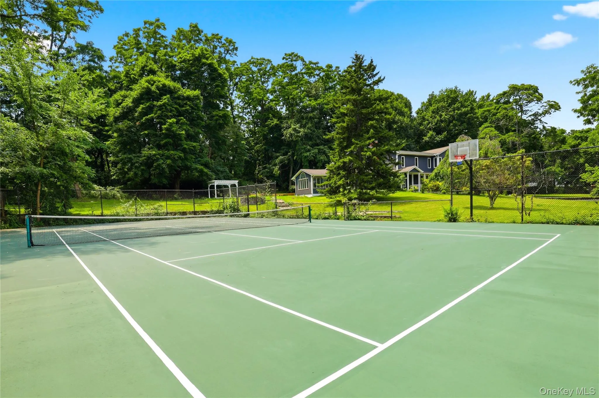 Full-size tennis court/basketball court featuring a green surface with white line markings Full-size tennis court/basketball court featuring a green surface with white line markings