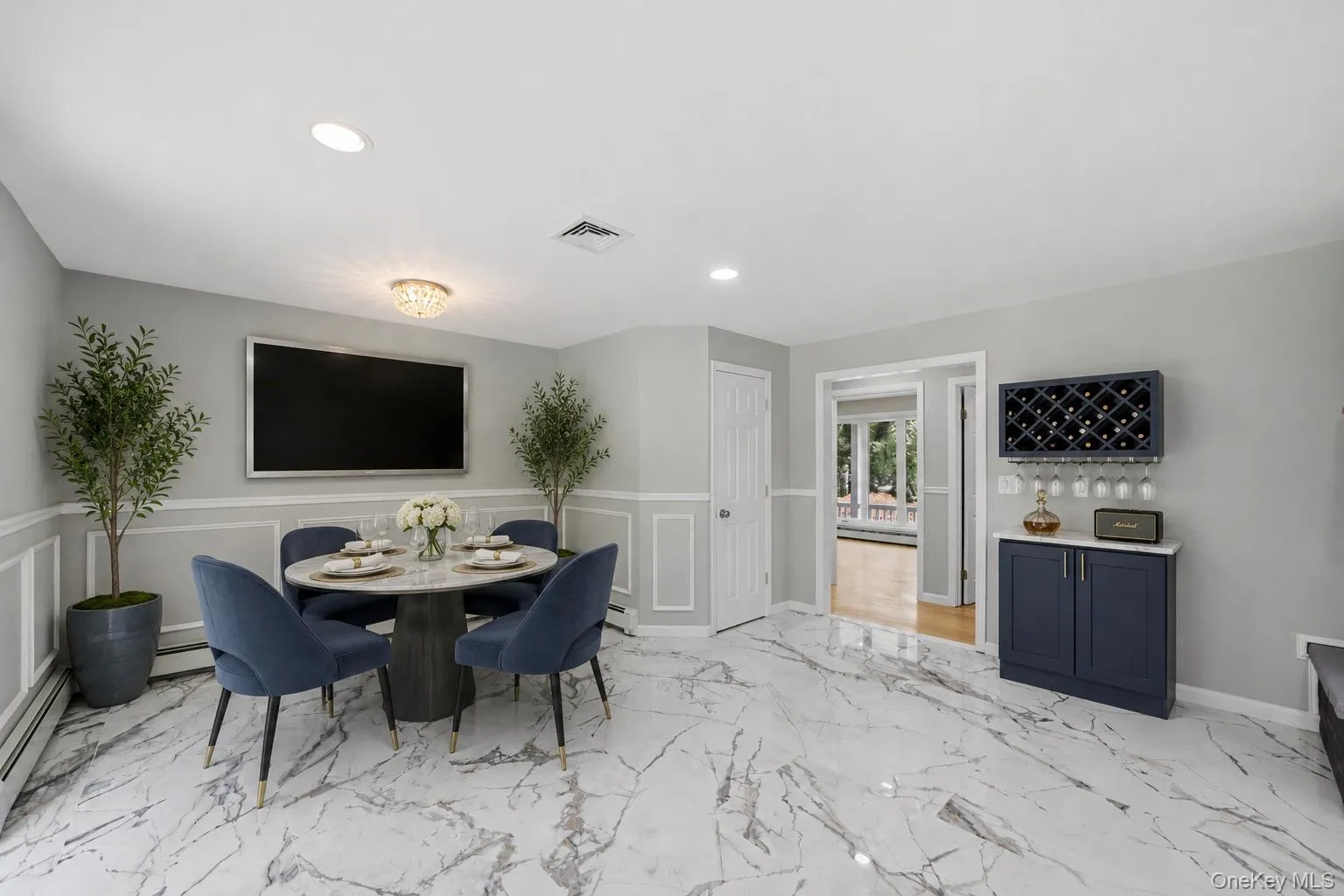 Spacious dining area featuring large format marble-look tile flooring, wainscoting details, a built-in beverage bar with wine storage, and a recessed ceiling light Spacious dining area featuring large format marble-look tile flooring, wainscoting details, a built-in beverage bar with wine storage, and a recessed ceiling light