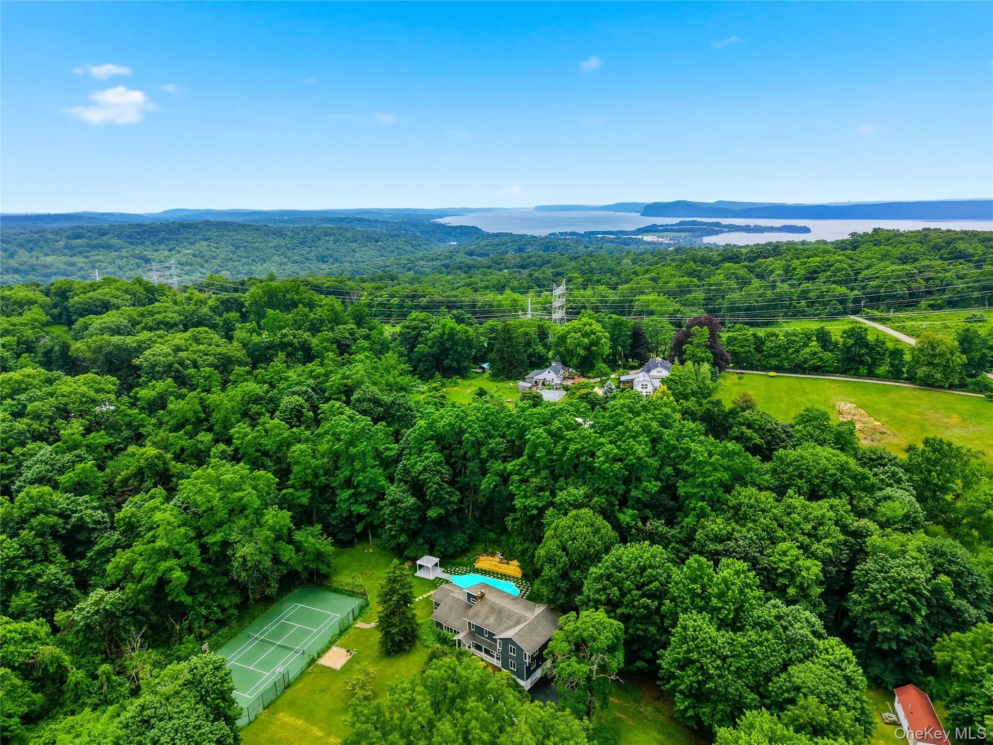Expansive property featuring a tennis court, swimming pool, and wooded surroundings Expansive property featuring a tennis court, swimming pool, and wooded surroundings