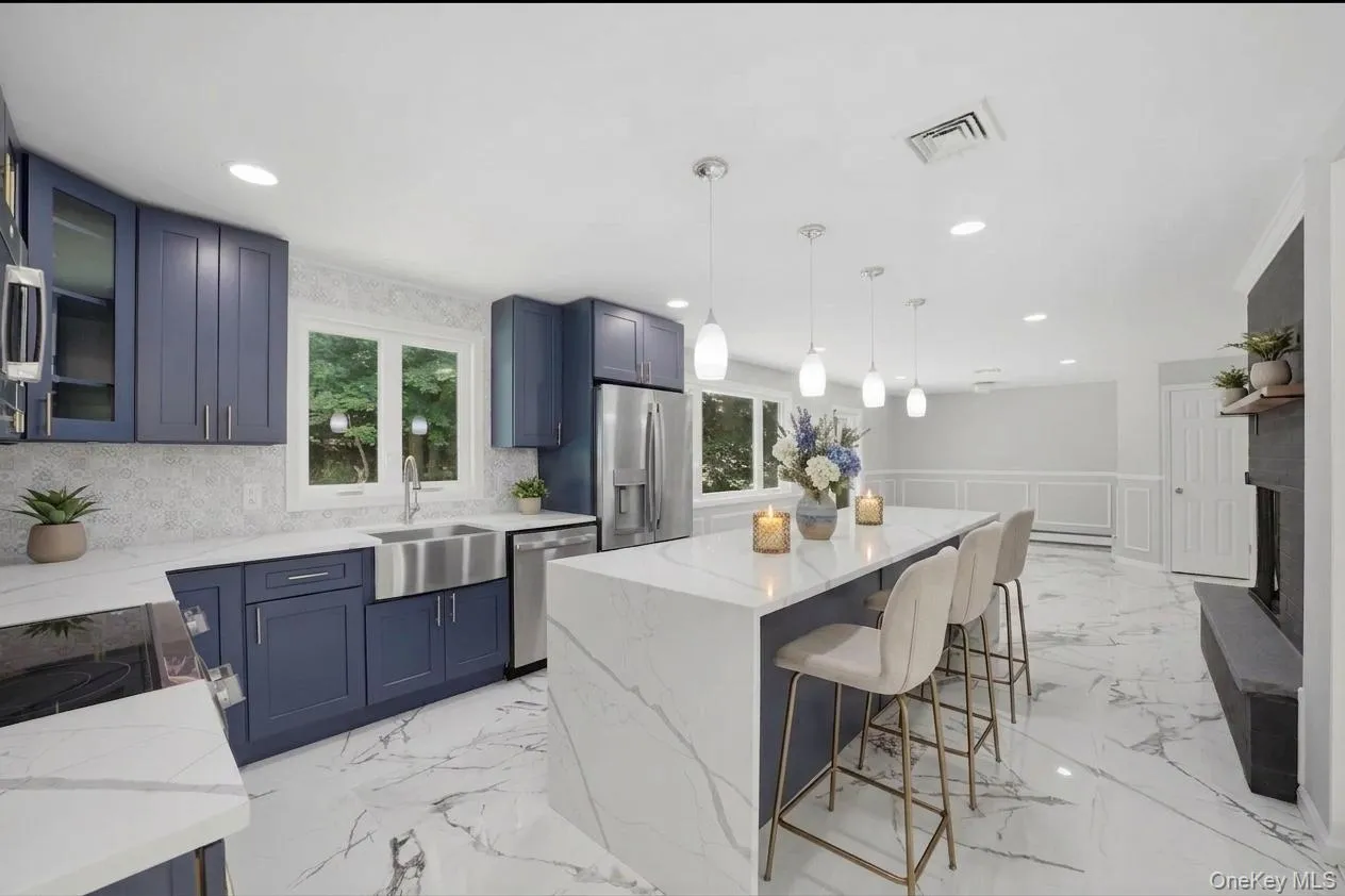 Open-concept kitchen featuring an expansive central island with a waterfall edge, quartz countertops, and blue shaker cabinetry Open-concept kitchen featuring an expansive central island with a waterfall edge, quartz countertops, and blue shaker cabinetry