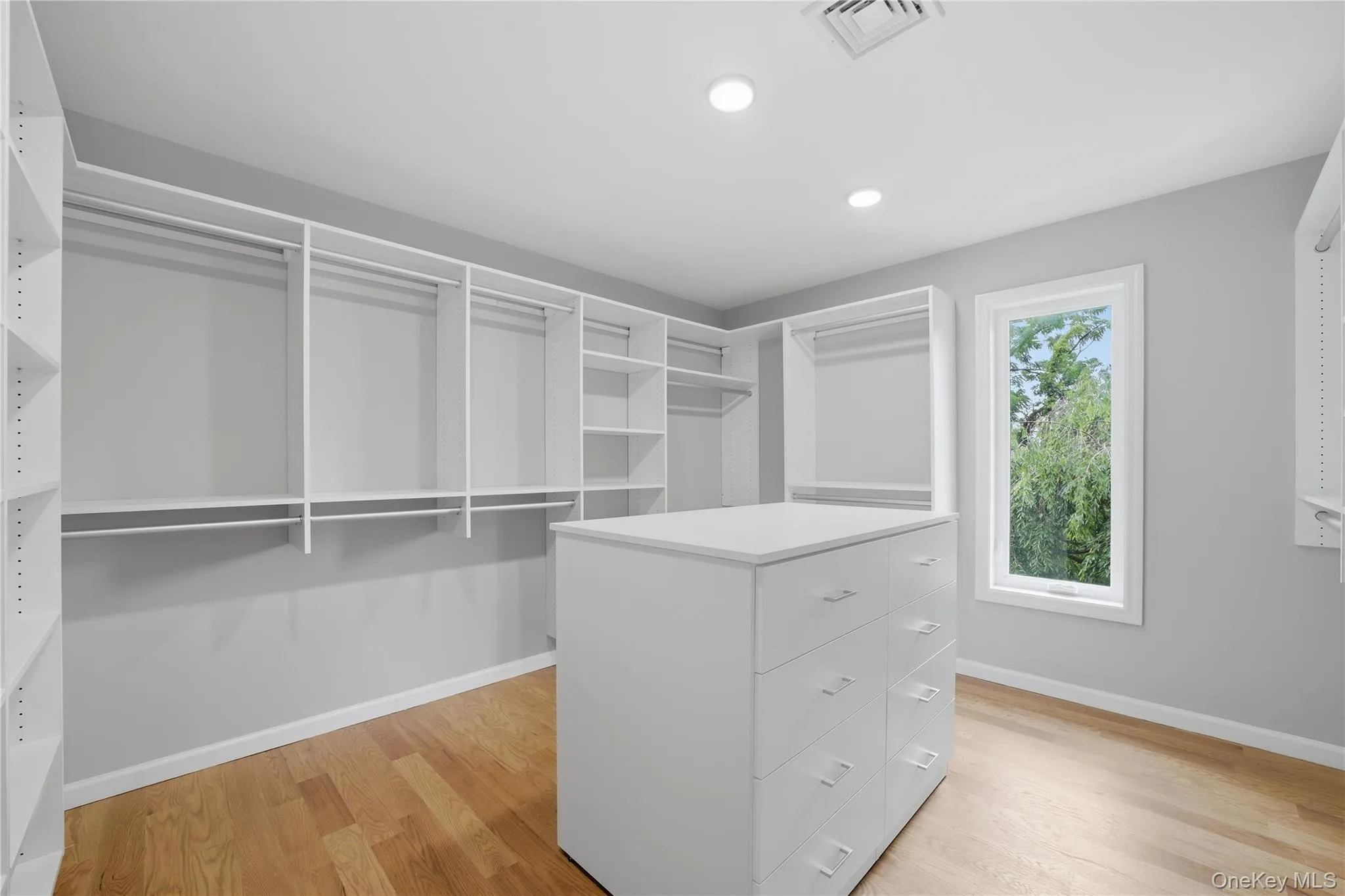 Walk-in closet with custom white shelving, multiple hanging rods, and a central island with integrated drawers Walk-in closet with custom white shelving, multiple hanging rods, and a central island with integrated drawers