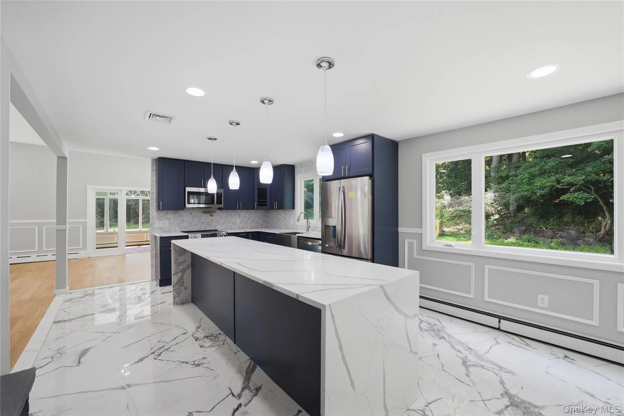 Kitchen featuring a large waterfall island with a light-toned countertop, dark blue cabinetry, stainless steel appliances, and marble-look tile flooring Kitchen featuring a large waterfall island with a light-toned countertop, dark blue cabinetry, stainless steel appliances, and marble-look tile flooring