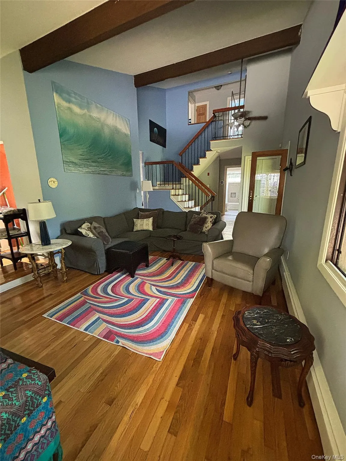 Front Living area featuring high ceilings with exposed wood beams, hardwood flooring, and a multi-level staircase with wood handrails and black metal balusters Front Living area featuring high ceilings with exposed wood beams, hardwood flooring, and a multi-level staircase with wood handrails and black metal balusters