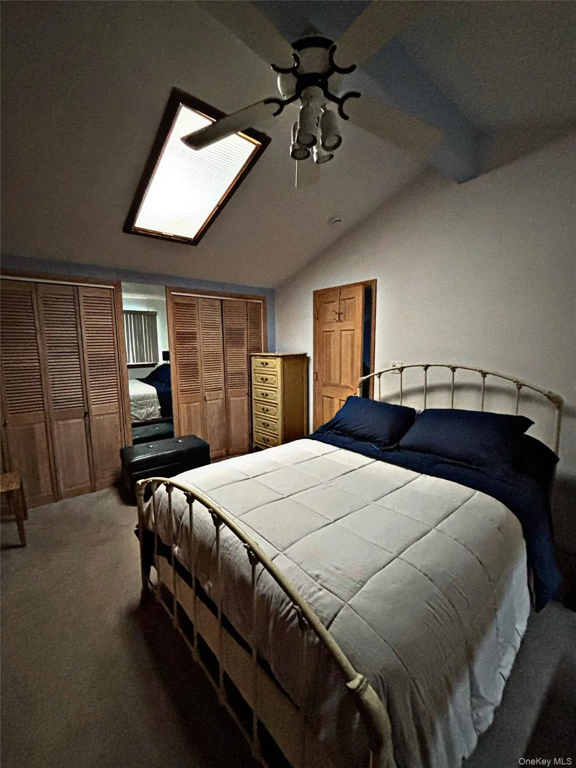 Bedroom featuring a vaulted ceiling with skylight, ceiling fan with light fixture, and wood louvered bifold closet doors Bedroom featuring a vaulted ceiling with skylight, ceiling fan with light fixture, and wood louvered bifold closet doors