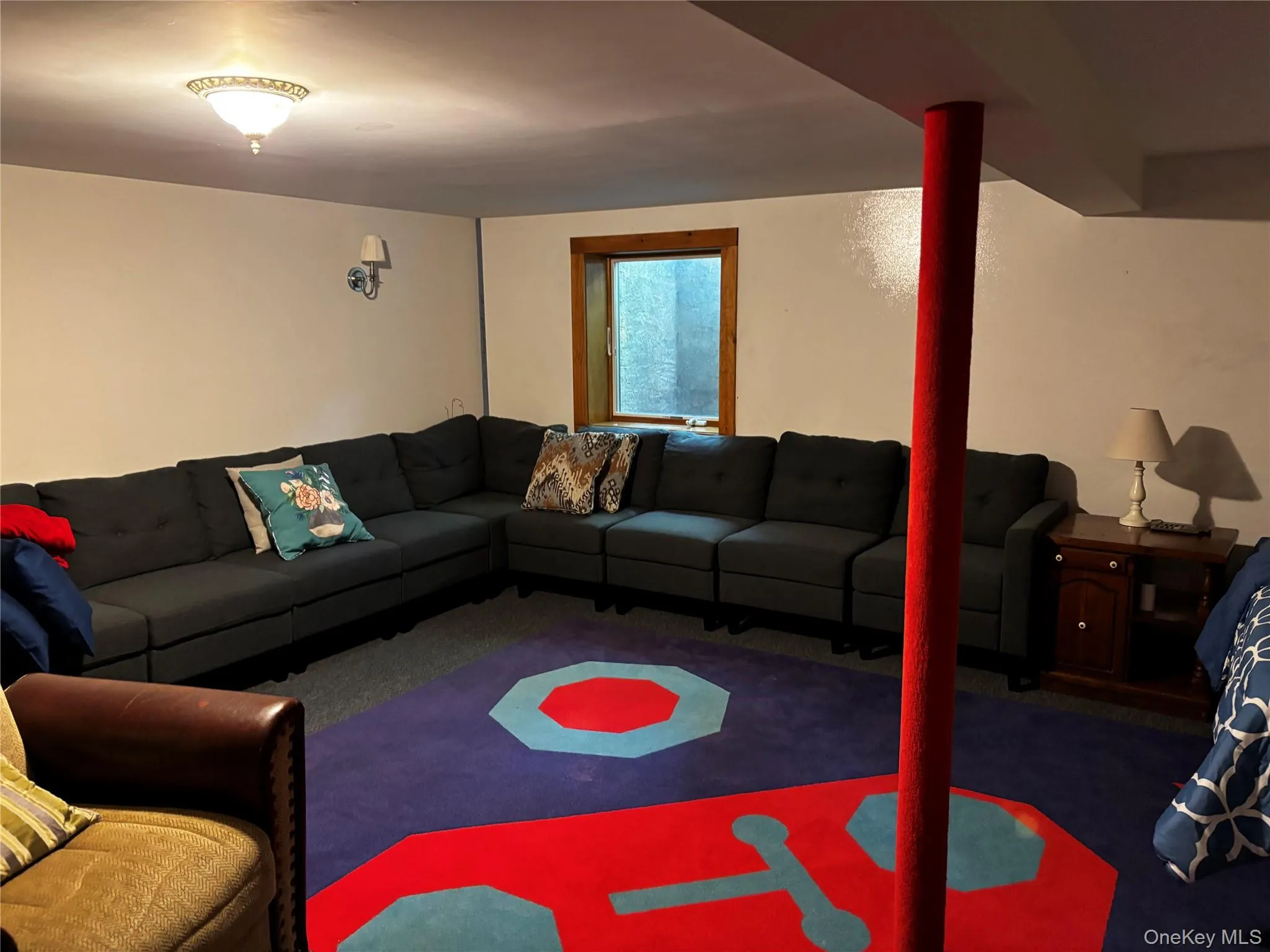 Lower-level room with a wood-framed window, wall sconce lighting, and a ceiling-mounted fixture Lower-level room with a wood-framed window, wall sconce lighting, and a ceiling-mounted fixture