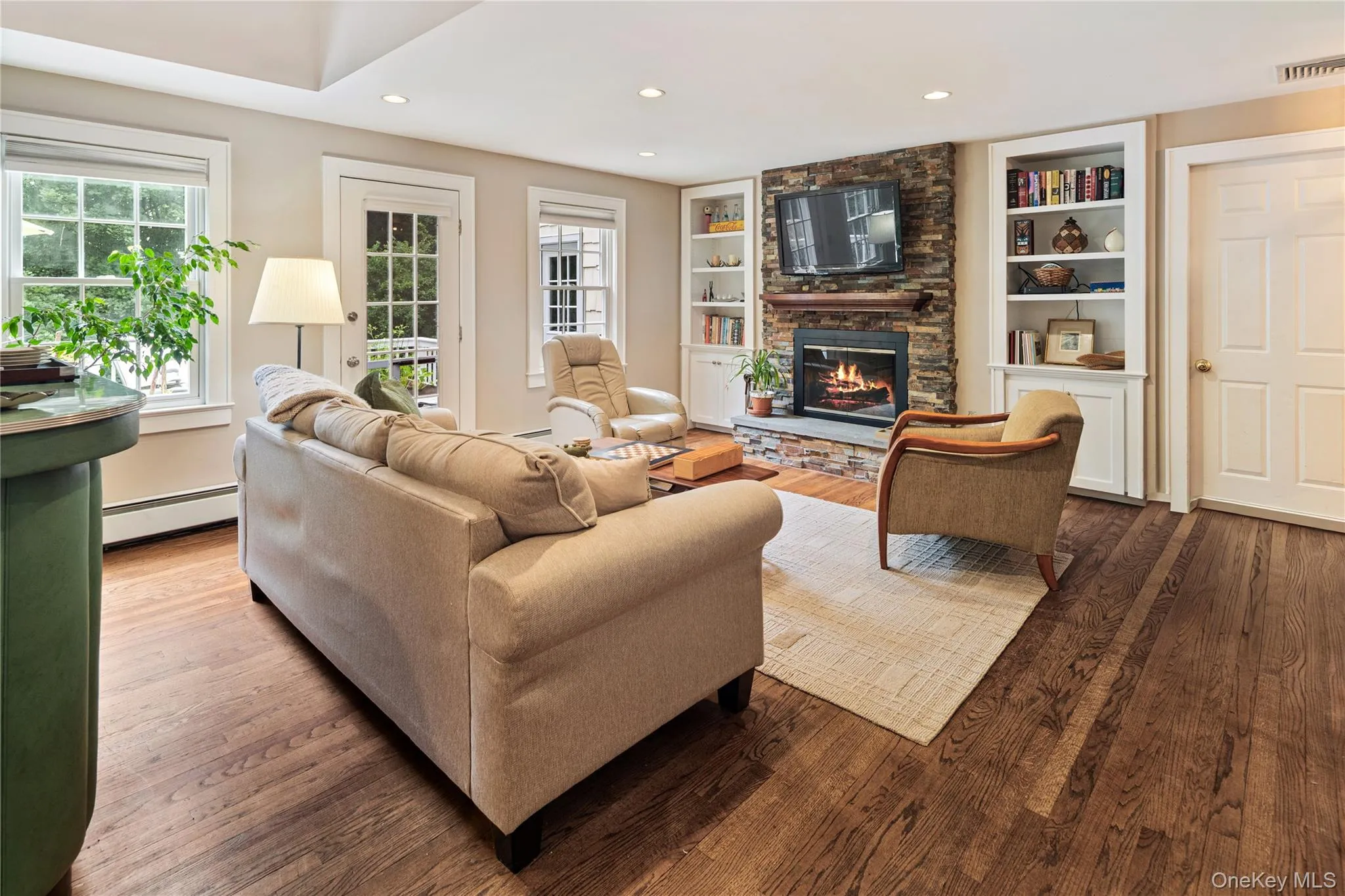 Family room with raised hearth stacked stone fireplace, flanked by built-in cupboards with shelving above, oak floors, recessed lighting, powder room, door to main floor garage, door to back deck Family room with raised hearth stacked stone fireplace, flanked by built-in cupboards with shelving above, oak floors, recessed lighting, powder room, door to main floor garage, door to back deck