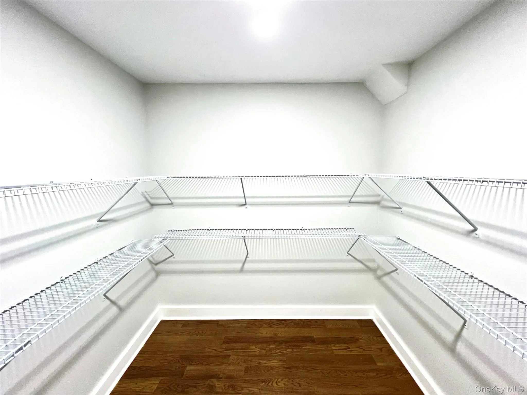 Walk-in closet featuring white wire shelving, white baseboards, and wood-finish flooring Walk-in closet featuring white wire shelving, white baseboards, and wood-finish flooring