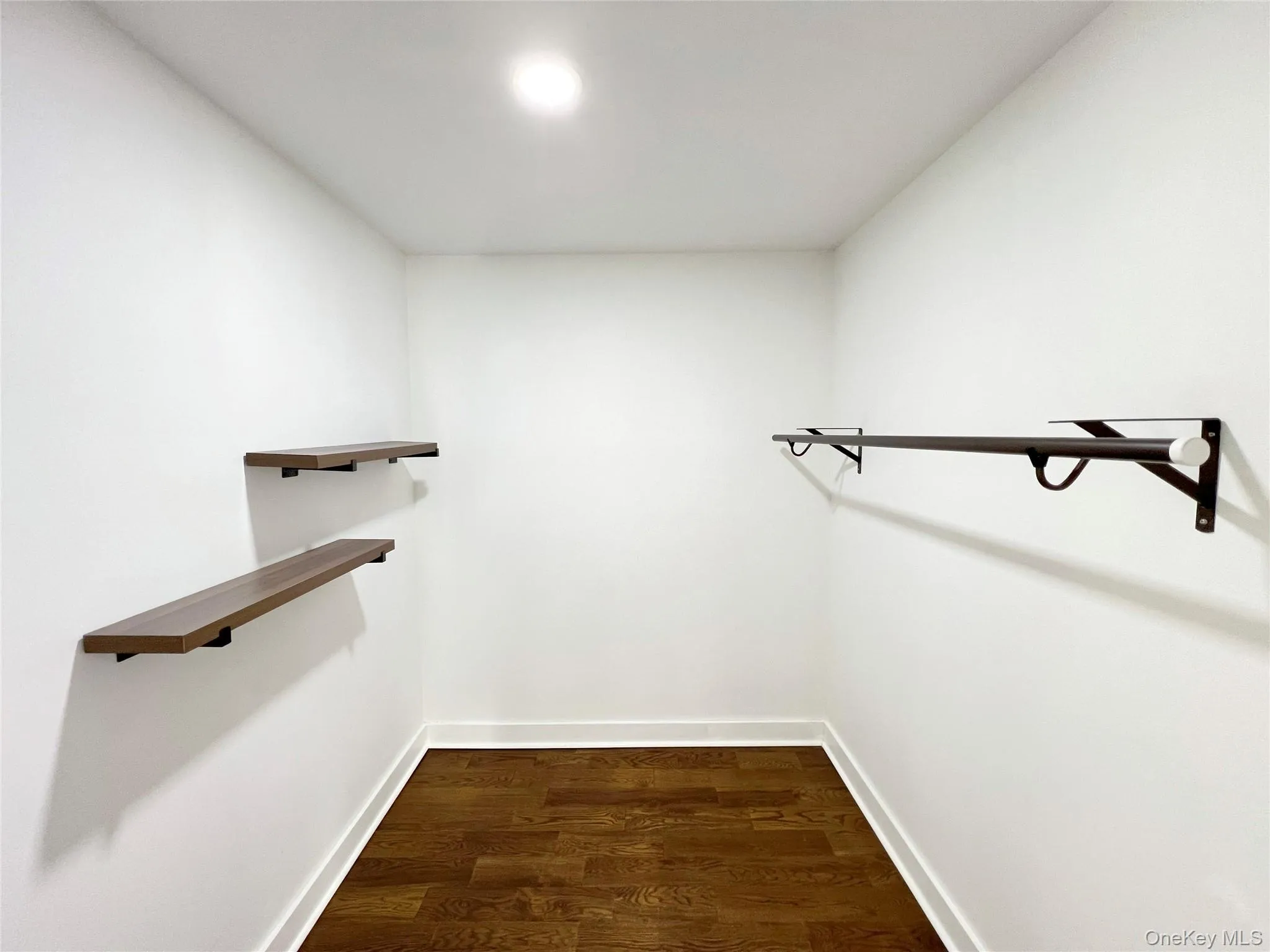 Walk-in closet featuring wood-finish flooring, recessed lighting, two floating wood-finish shelves, and a dark-toned hanging rod Walk-in closet featuring wood-finish flooring, recessed lighting, two floating wood-finish shelves, and a dark-toned hanging rod