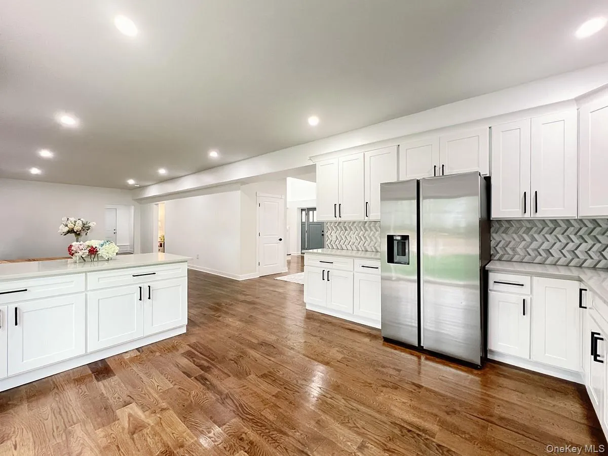 Spacious kitchen featuring white shaker cabinetry, stainless steel refrigerator, herringbone tile backsplash, and light-tone countertops Spacious kitchen featuring white shaker cabinetry, stainless steel refrigerator, herringbone tile backsplash, and light-tone countertops