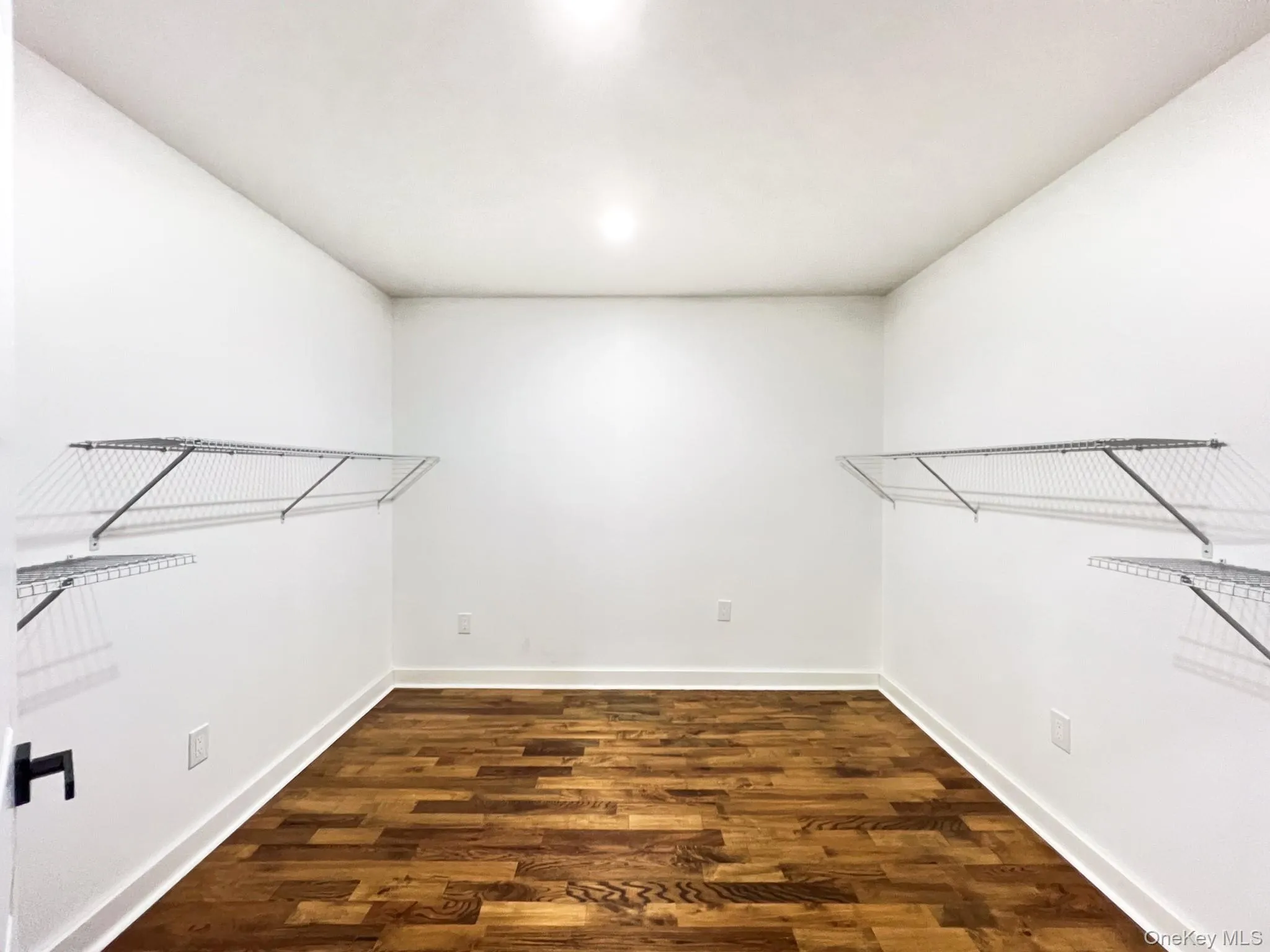Spacious walk-in closet featuring wood flooring, white walls, and built-in wire shelving Spacious walk-in closet featuring wood flooring, white walls, and built-in wire shelving