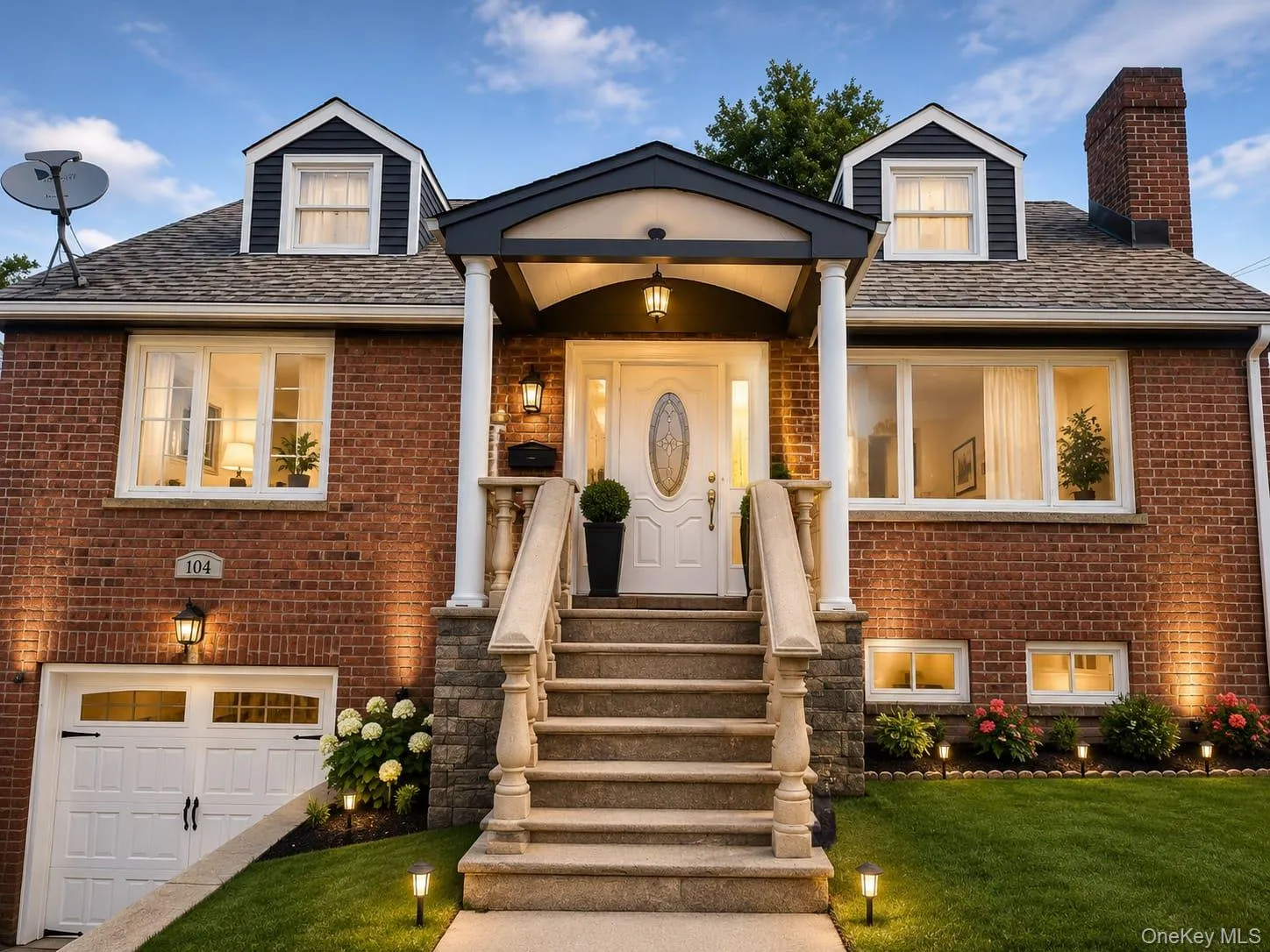 Brick facade residence featuring a covered entry porch, stone staircase with balustrades, integrated garage, and dormer windows Brick facade residence featuring a covered entry porch, stone staircase with balustrades, integrated garage, and dormer windows