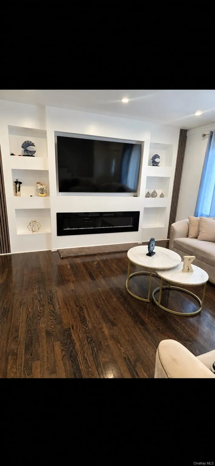 Built-in media center featuring an electric fireplace and recessed shelving, dark wood-finish flooring, and recessed ceiling lighting Built-in media center featuring an electric fireplace and recessed shelving, dark wood-finish flooring, and recessed ceiling lighting