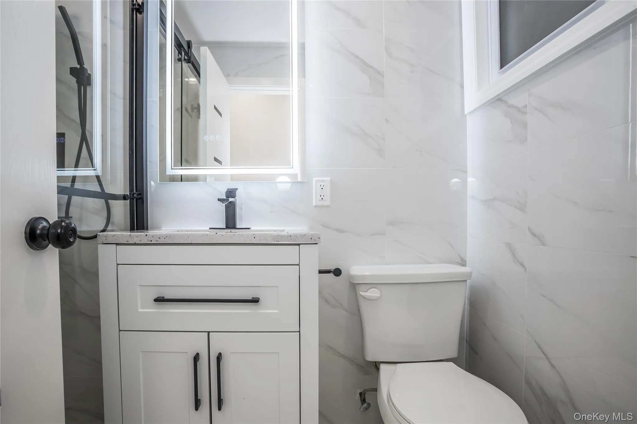 Bathroom with toilet, vanity, tile walls, and a shower Bathroom with toilet, vanity, tile walls, and a shower