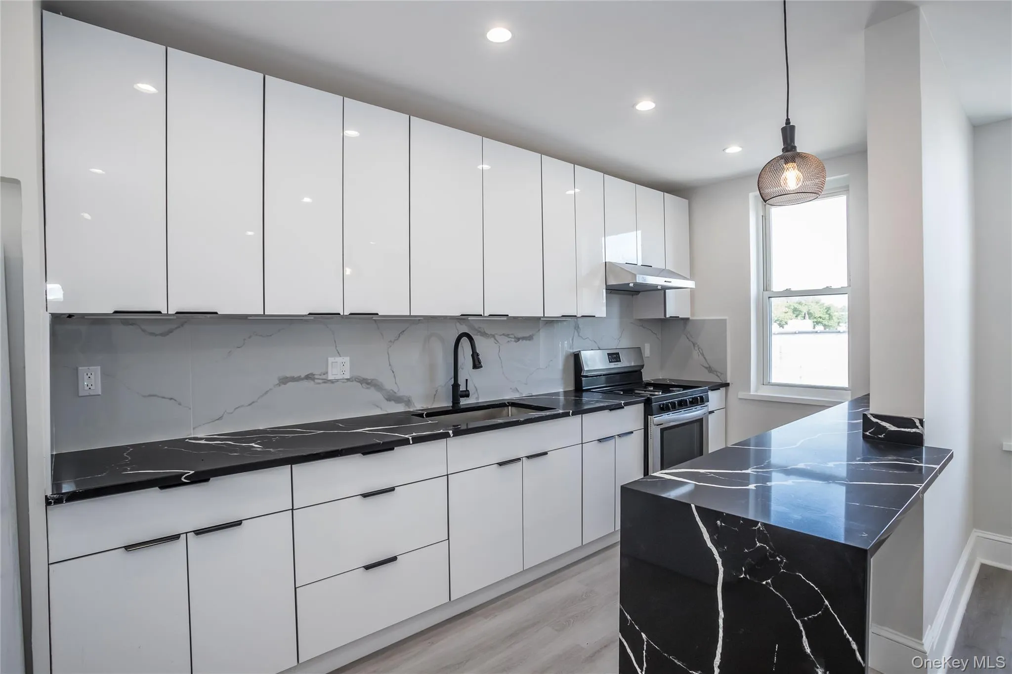 Kitchen featuring stainless steel gas range oven, under cabinet range hood, a sink, light wood-style floors, and white cabinetry Kitchen featuring stainless steel gas range oven, under cabinet range hood, a sink, light wood-style floors, and white cabinetry