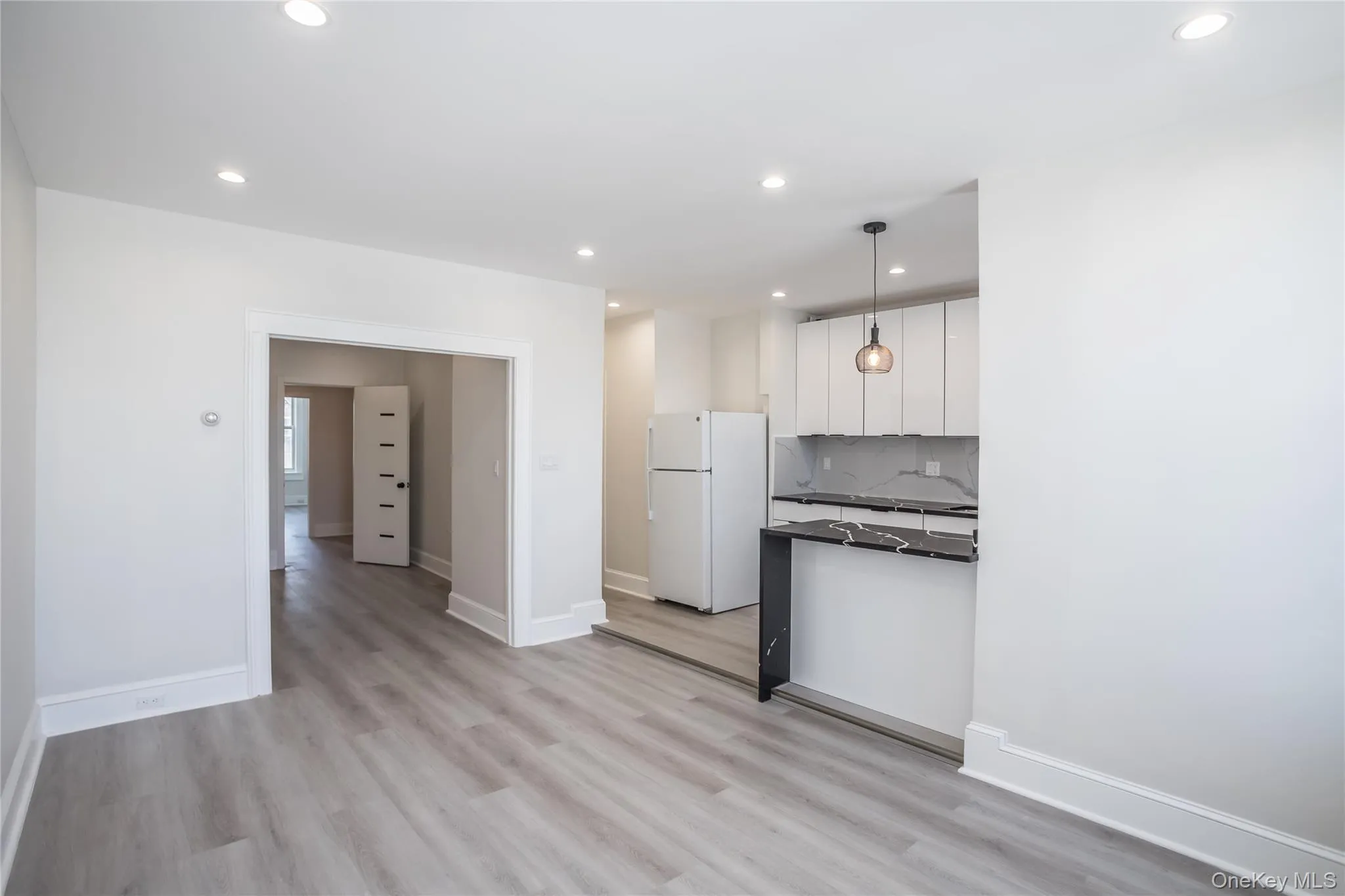Kitchen with freestanding refrigerator, dark countertops, white cabinets, recessed lighting, and light wood-style floors Kitchen with freestanding refrigerator, dark countertops, white cabinets, recessed lighting, and light wood-style floors