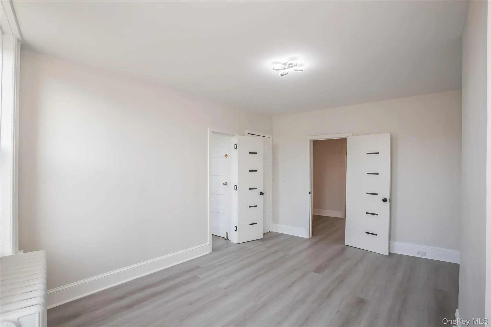 Unfurnished bedroom featuring radiator heating unit, light wood finished floors, and baseboards Unfurnished bedroom featuring radiator heating unit, light wood finished floors, and baseboards