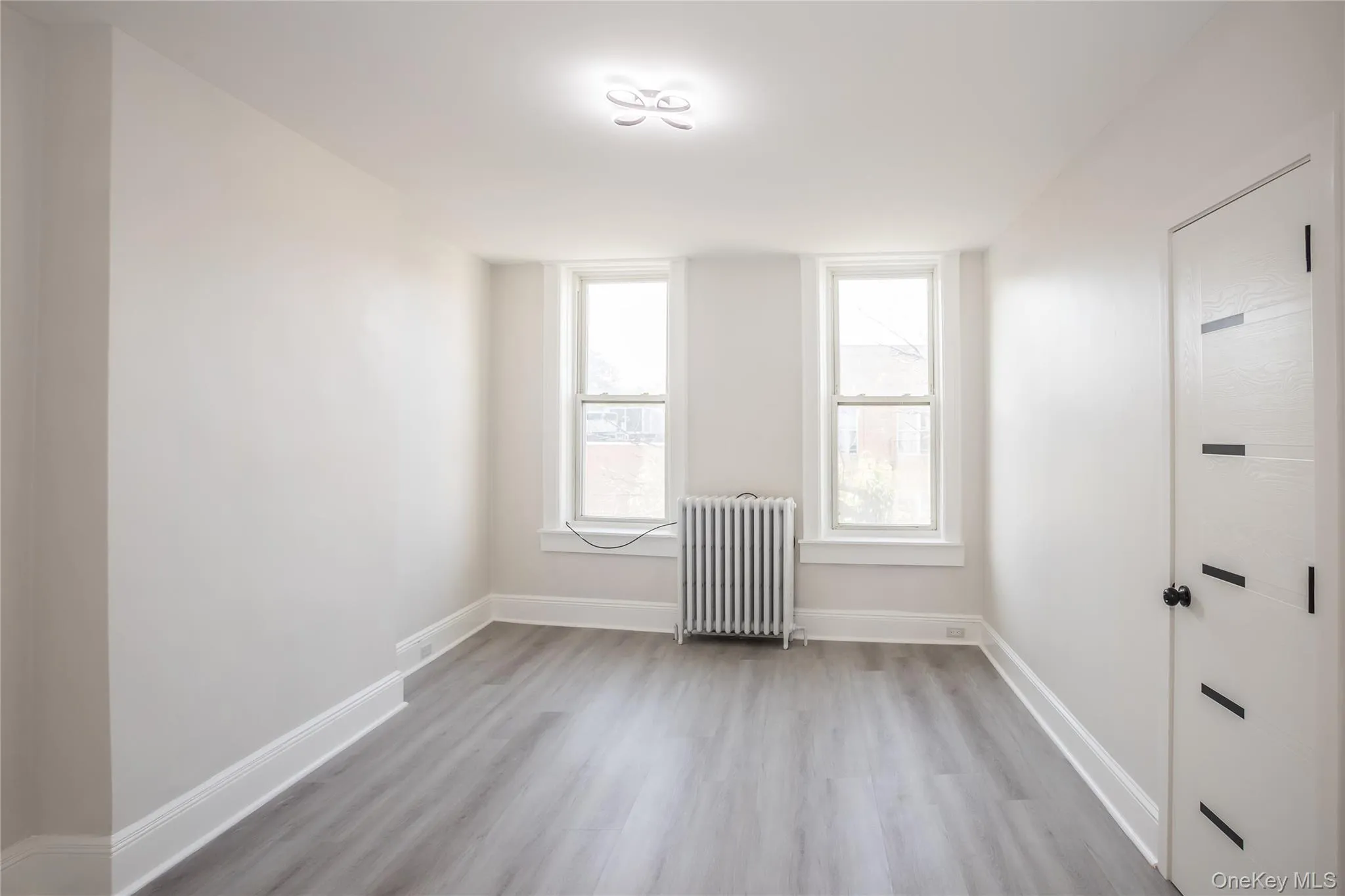 Empty room featuring radiator heating unit, wood finished floors, and baseboards Empty room featuring radiator heating unit, wood finished floors, and baseboards